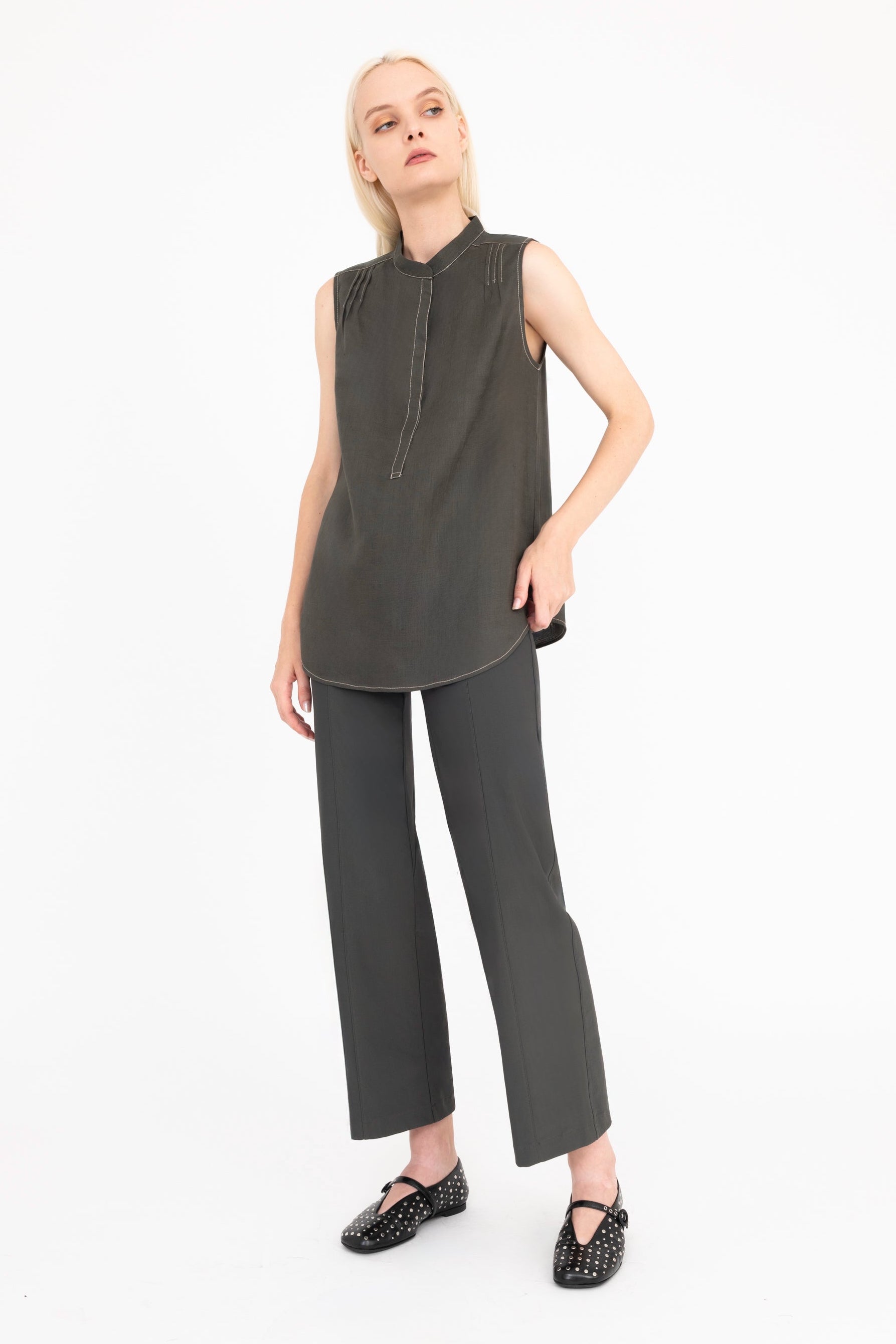 Woman wearing a sleeveless dark green top and matching pants on a white background