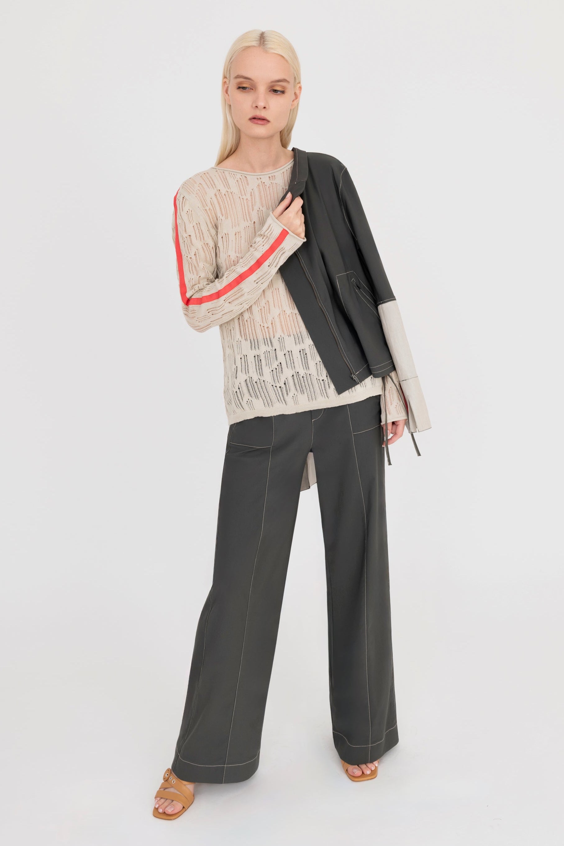 Woman wearing a beige sweater and pine green pants holding a pine green jacket on a white background