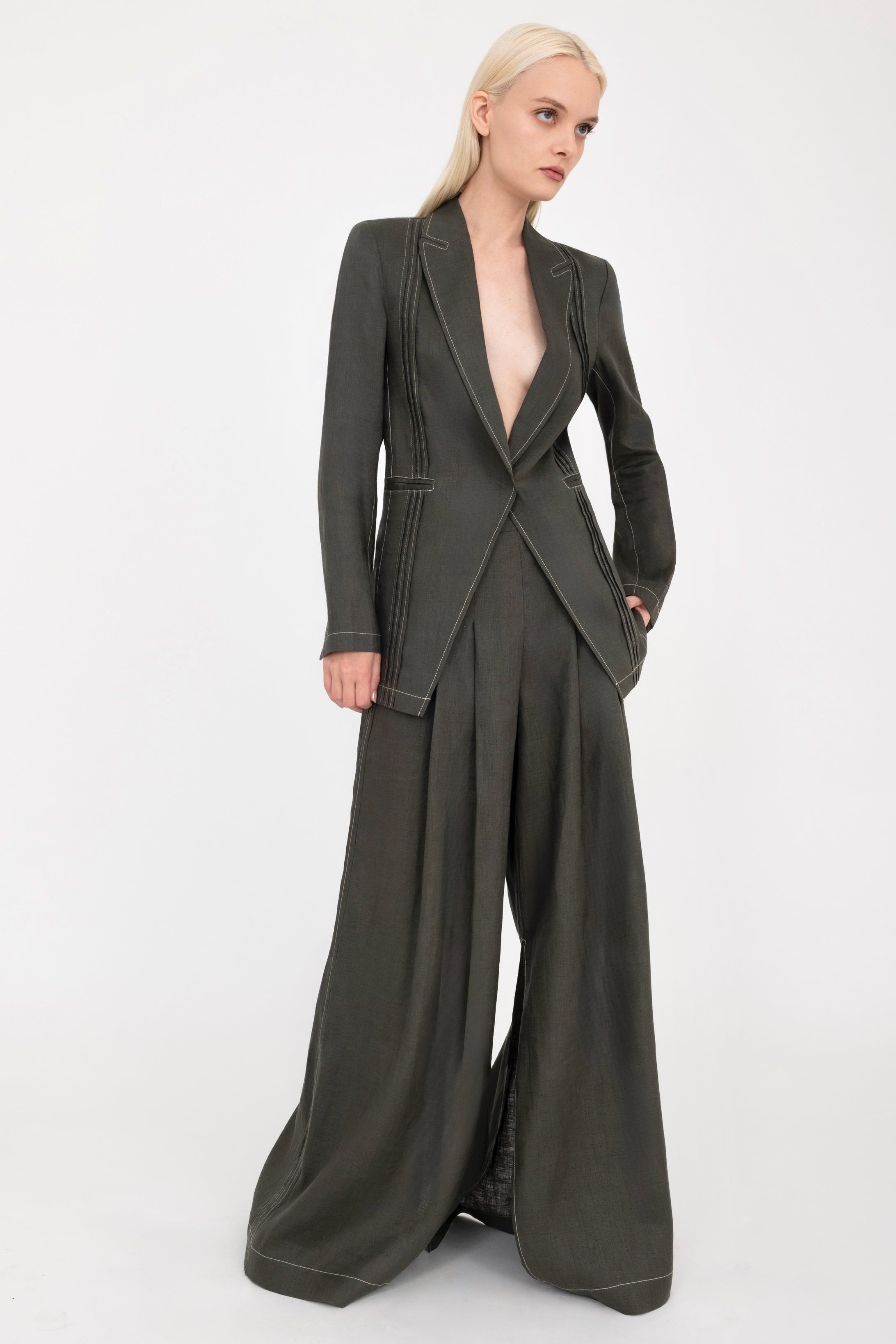Woman wearing a pine green  blazer and wide-leg pants with a white background