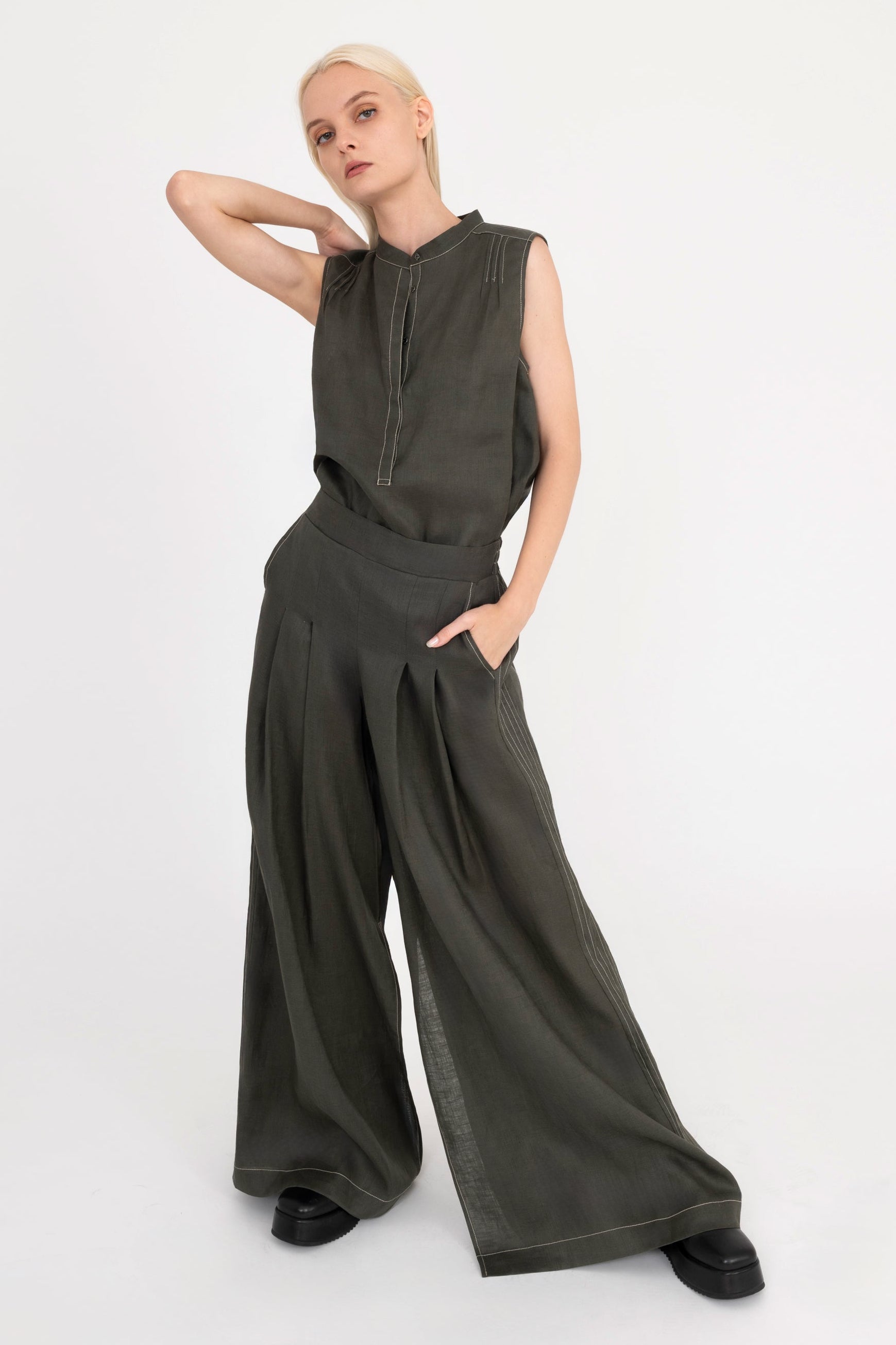 Woman wearing a sleeveless pine green top and wide-leg pants on a white background