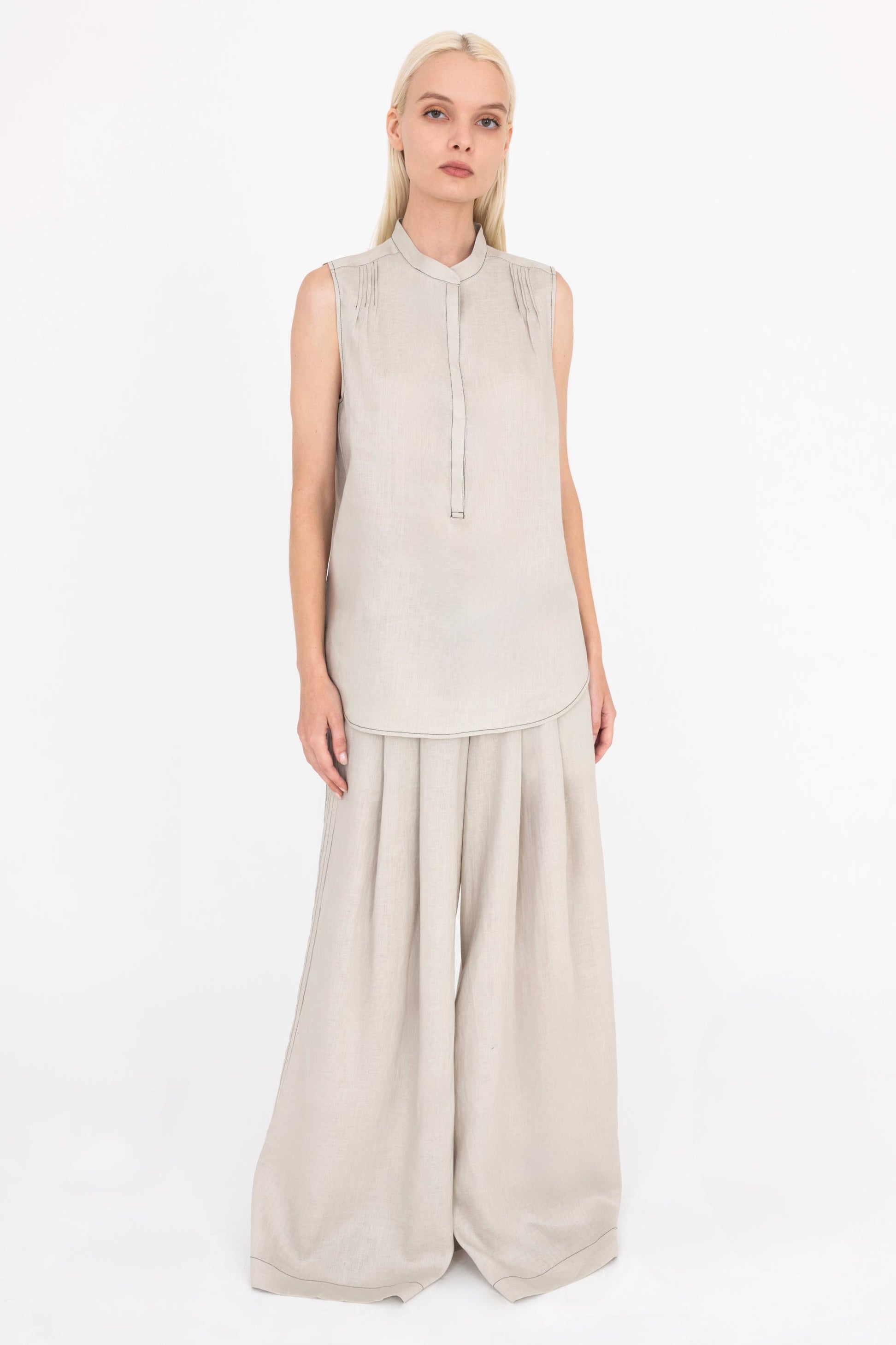 Woman wearing a sleeveless beige top and wide-leg pants on a white background