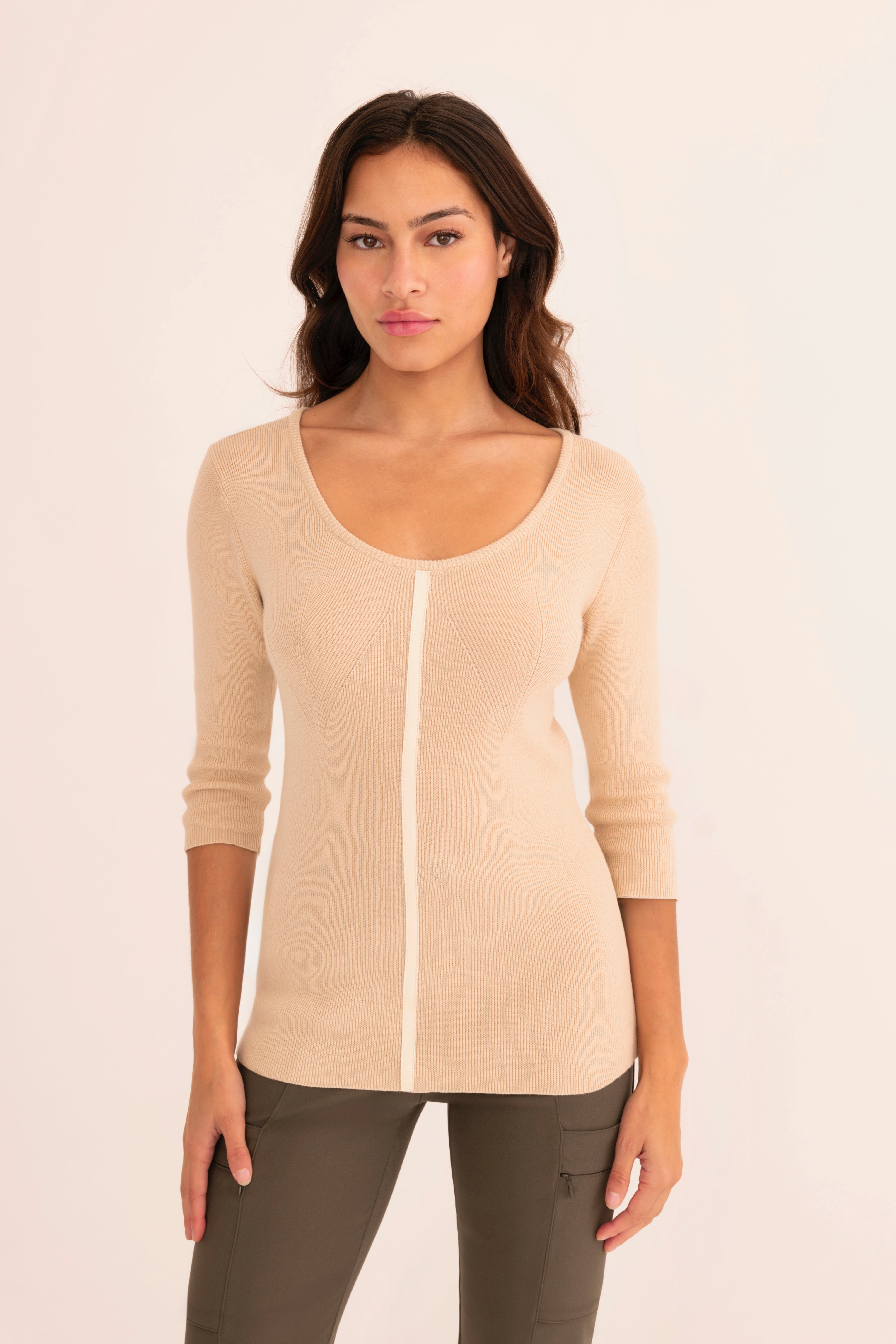 Front view of woman wearing a beige top and green pants on a white background