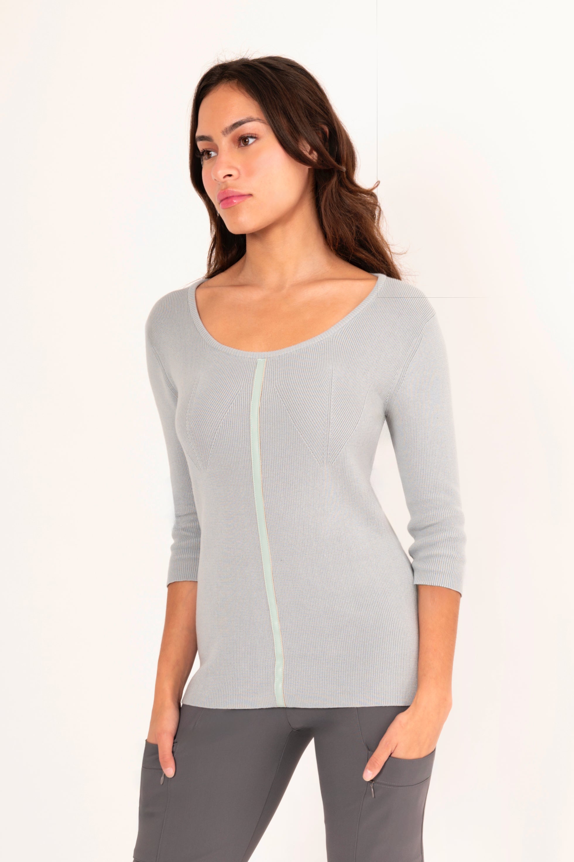 Side view of woman wearing a light blue top and gray pants on a white background