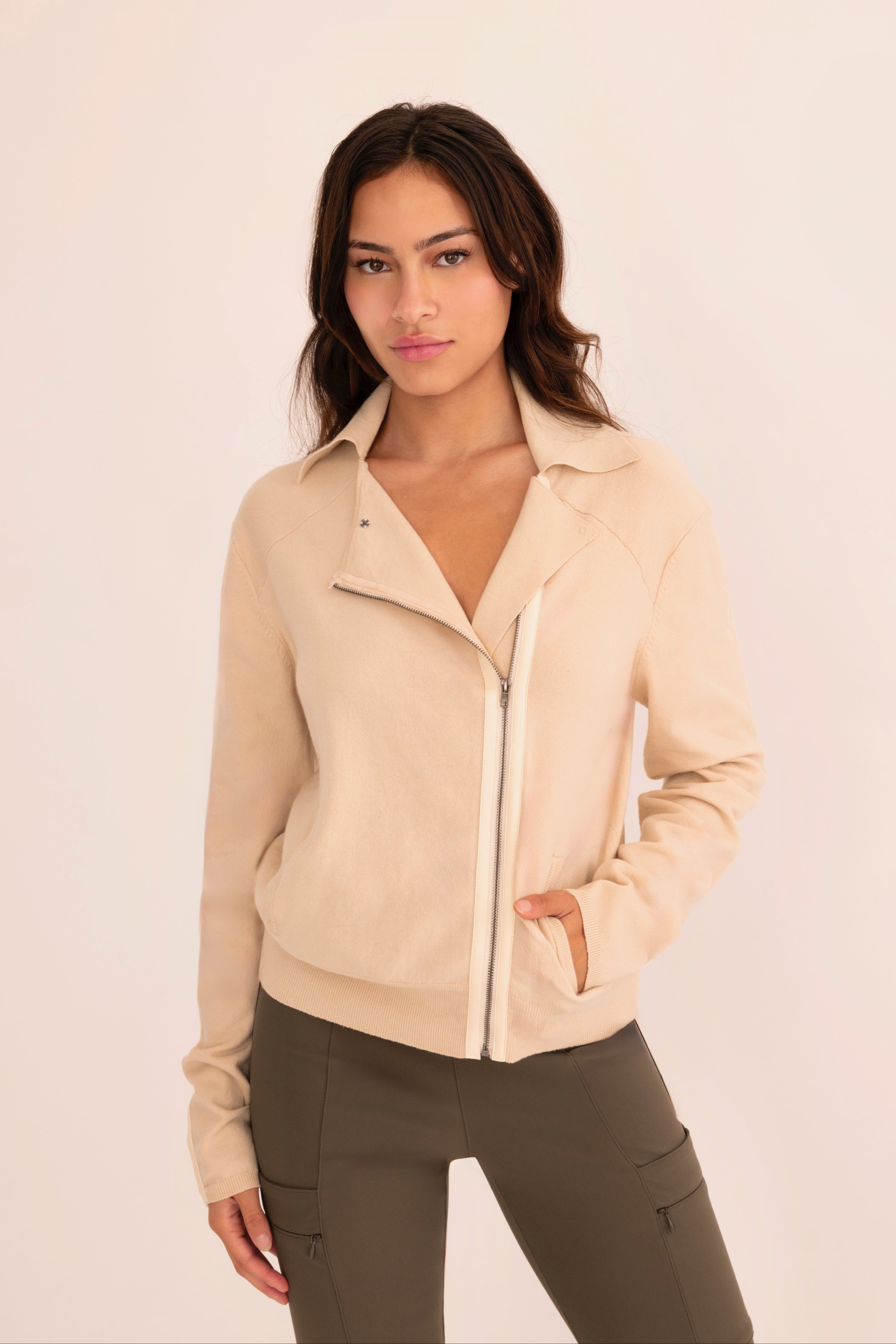 Front view of woman wearing a  beige zip-up jacket and green pants on a white background