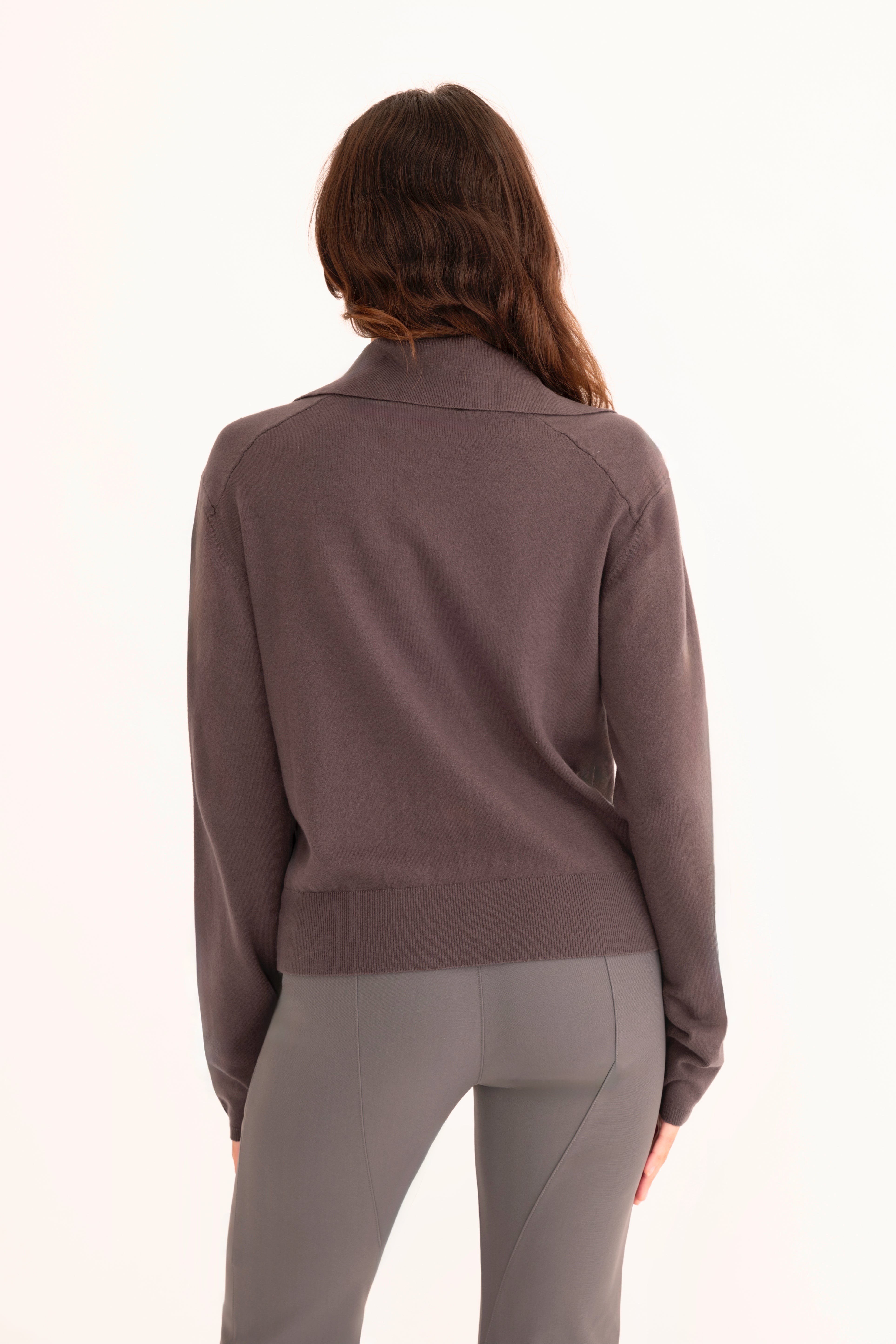 Back view of woman wearing a gray zip-up jacket and pants on a white background