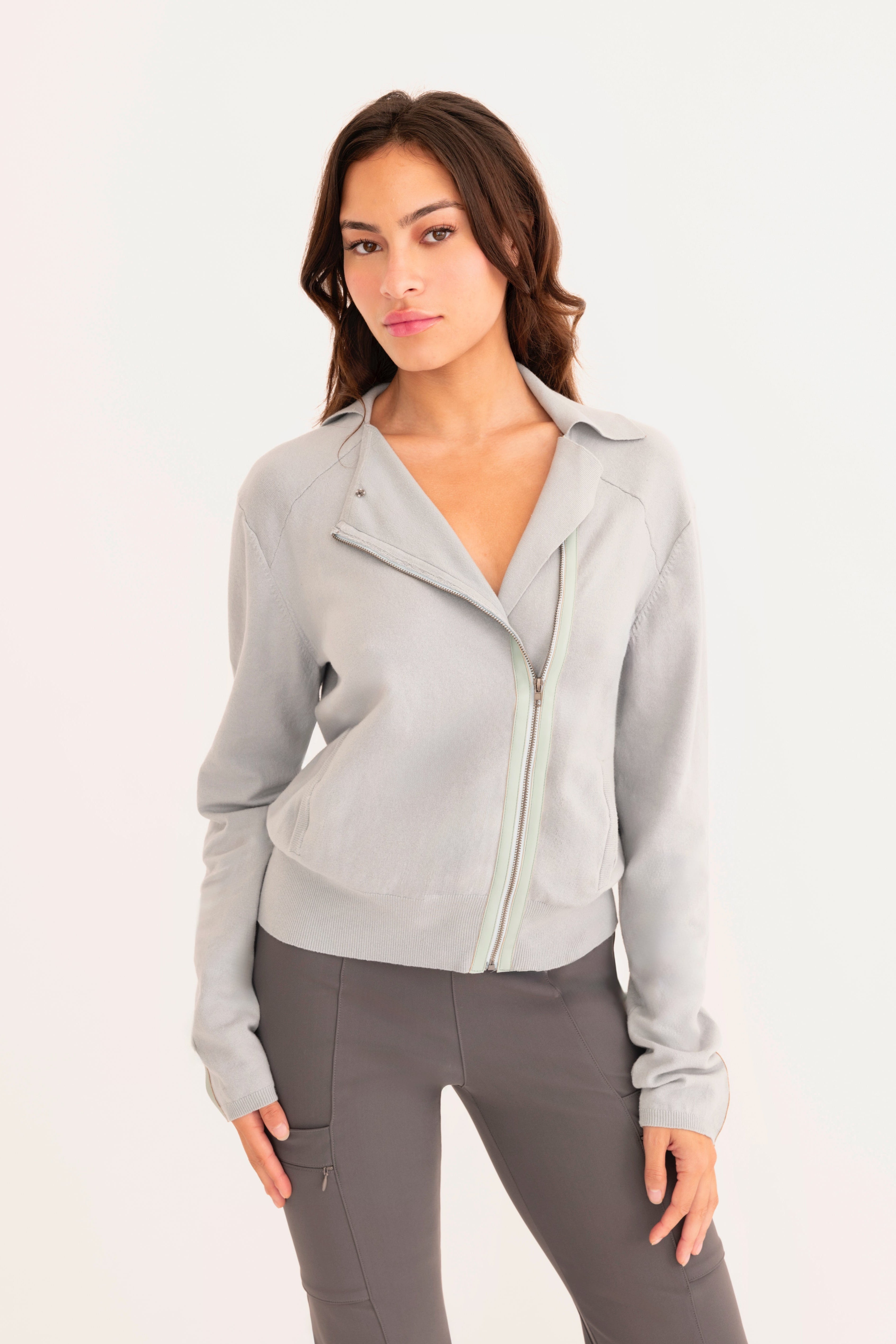 Front view of woman wearing a light  blue zip-up jacket and gray pants on a white background
