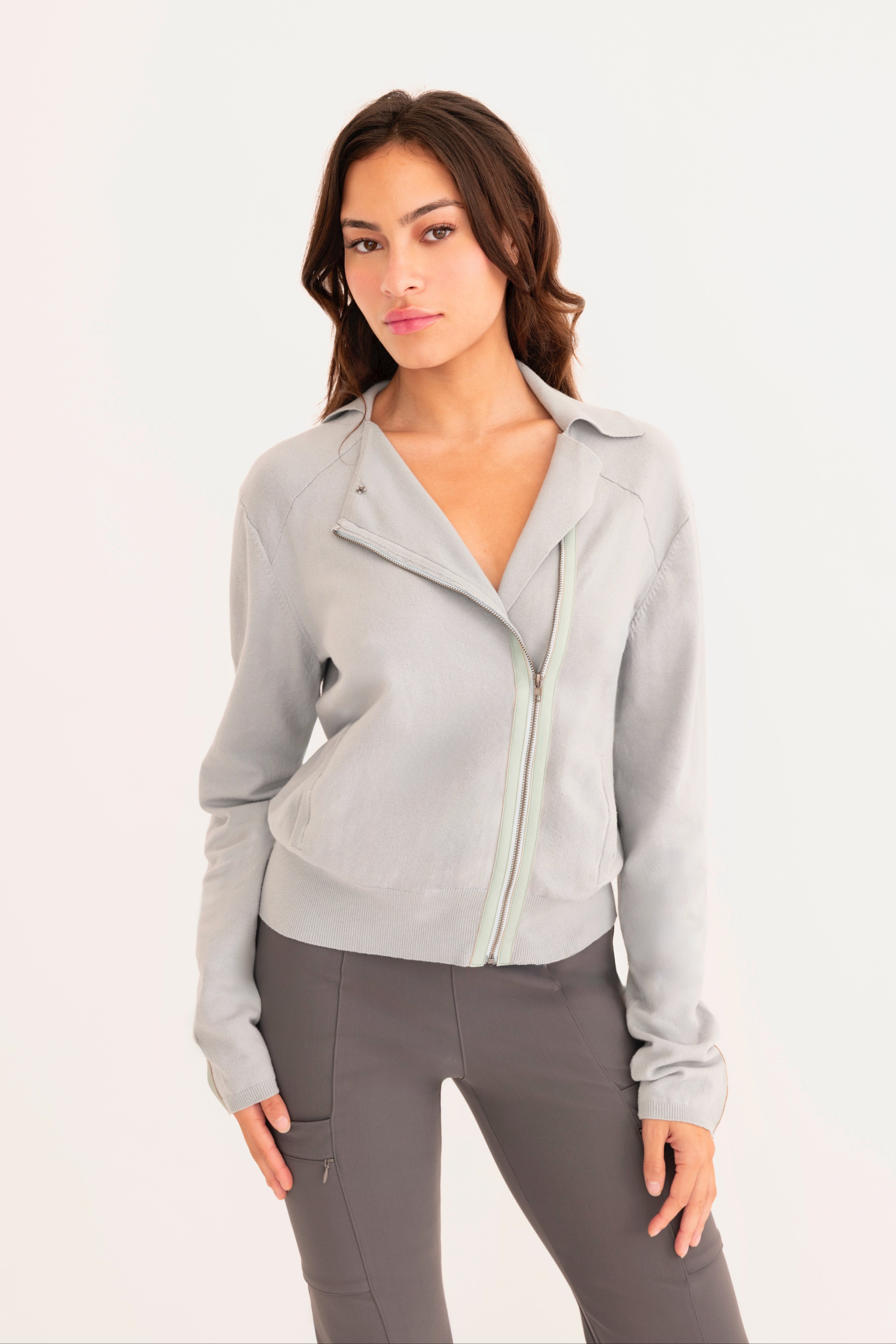 Front view of woman wearing a light  blue zip-up jacket and gray pants on a white background