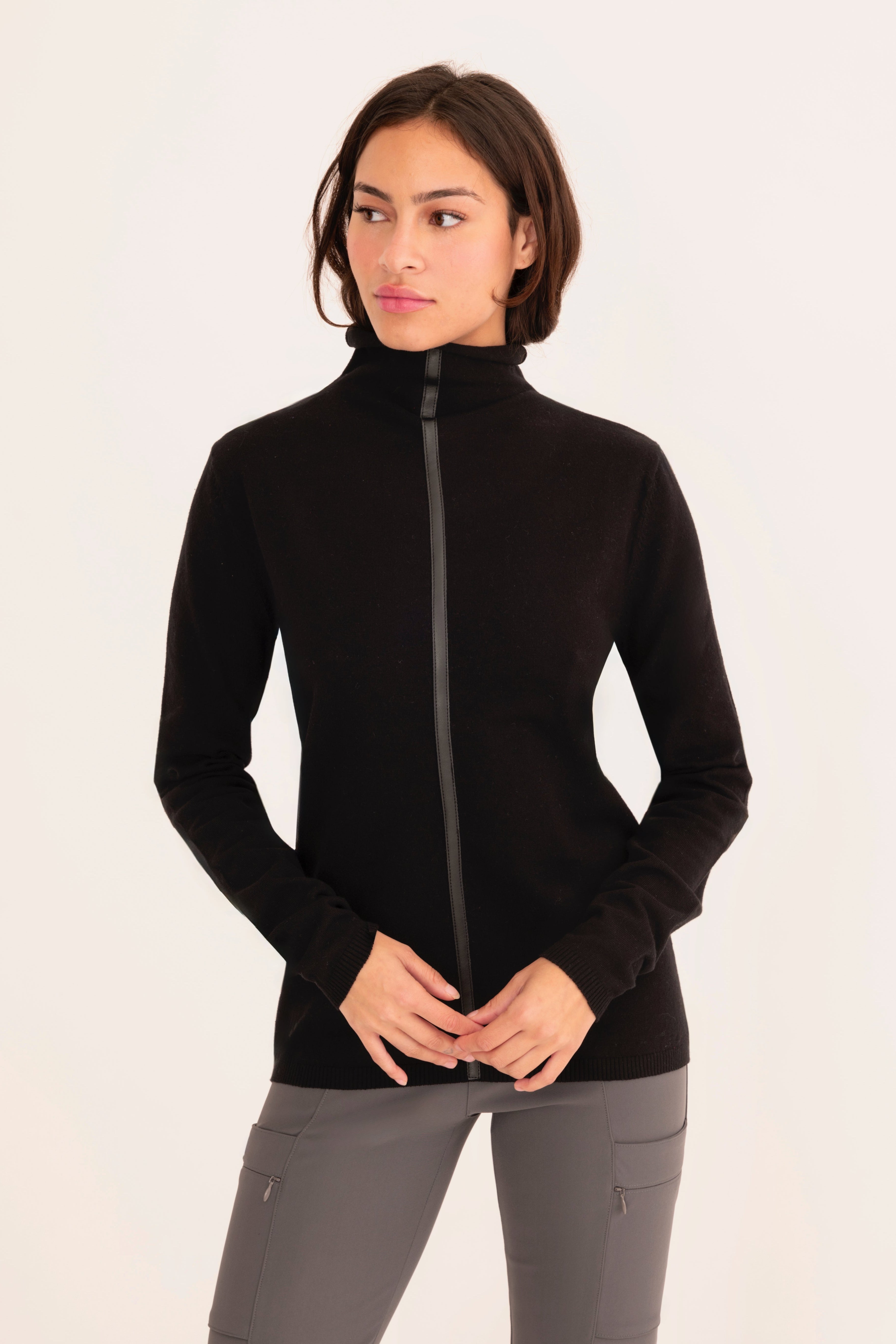Front view of a woman wearing a black funnel neck top and gray pants on a white background