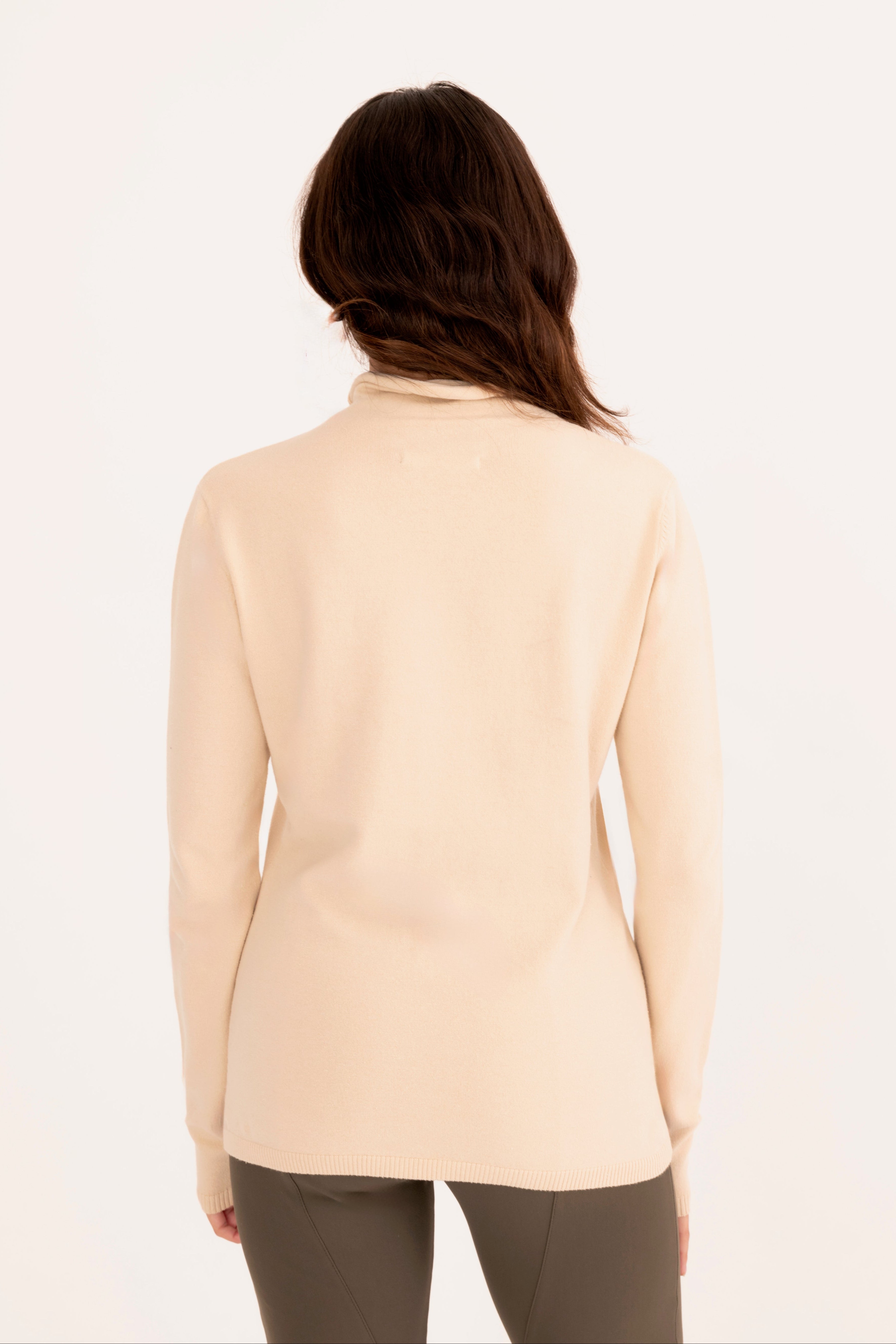Back view of a woman wearing a beige funnel neck top and gray pants on a white background