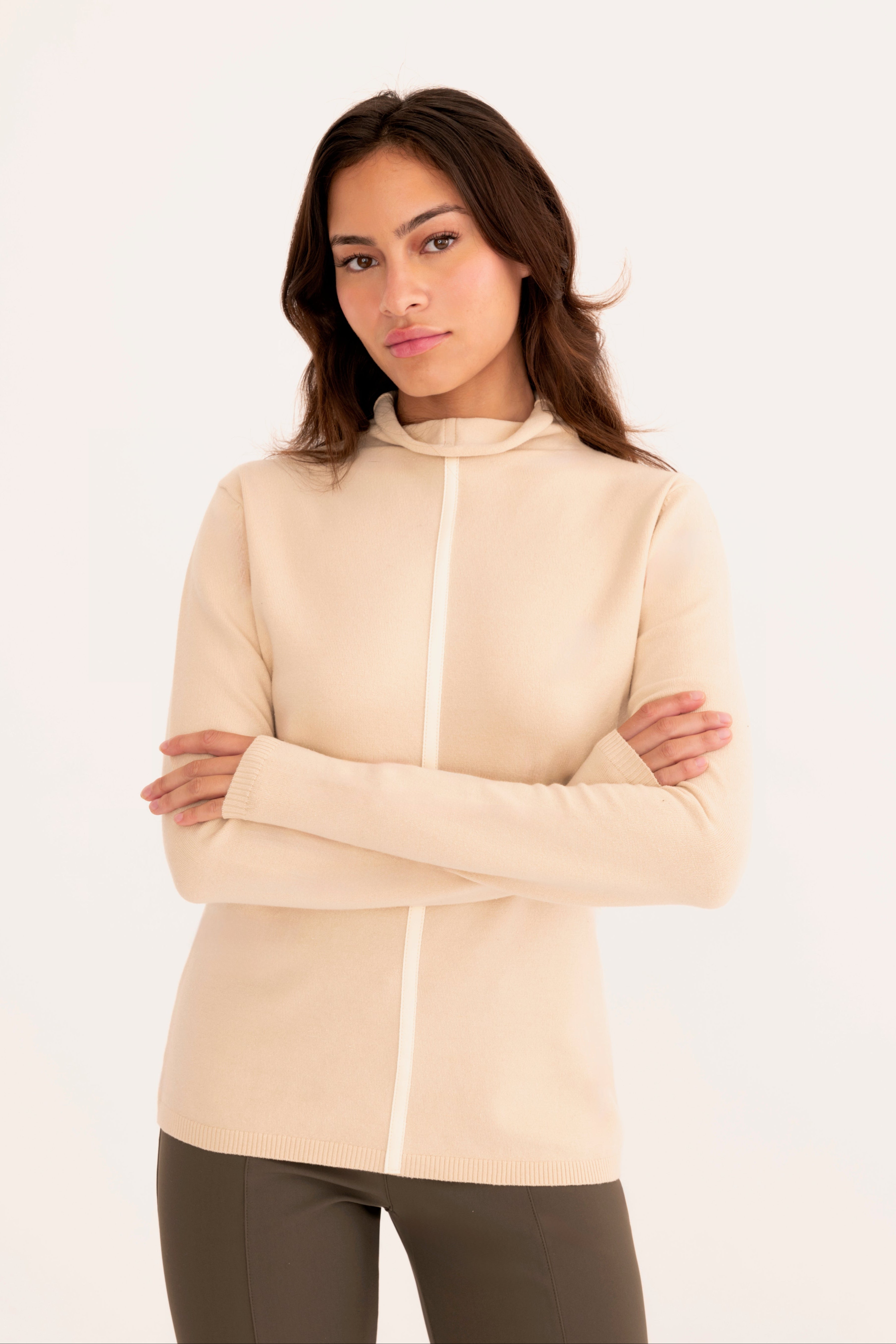 Front view of a woman wearing a beige funnel neck top and gray pants on a white background