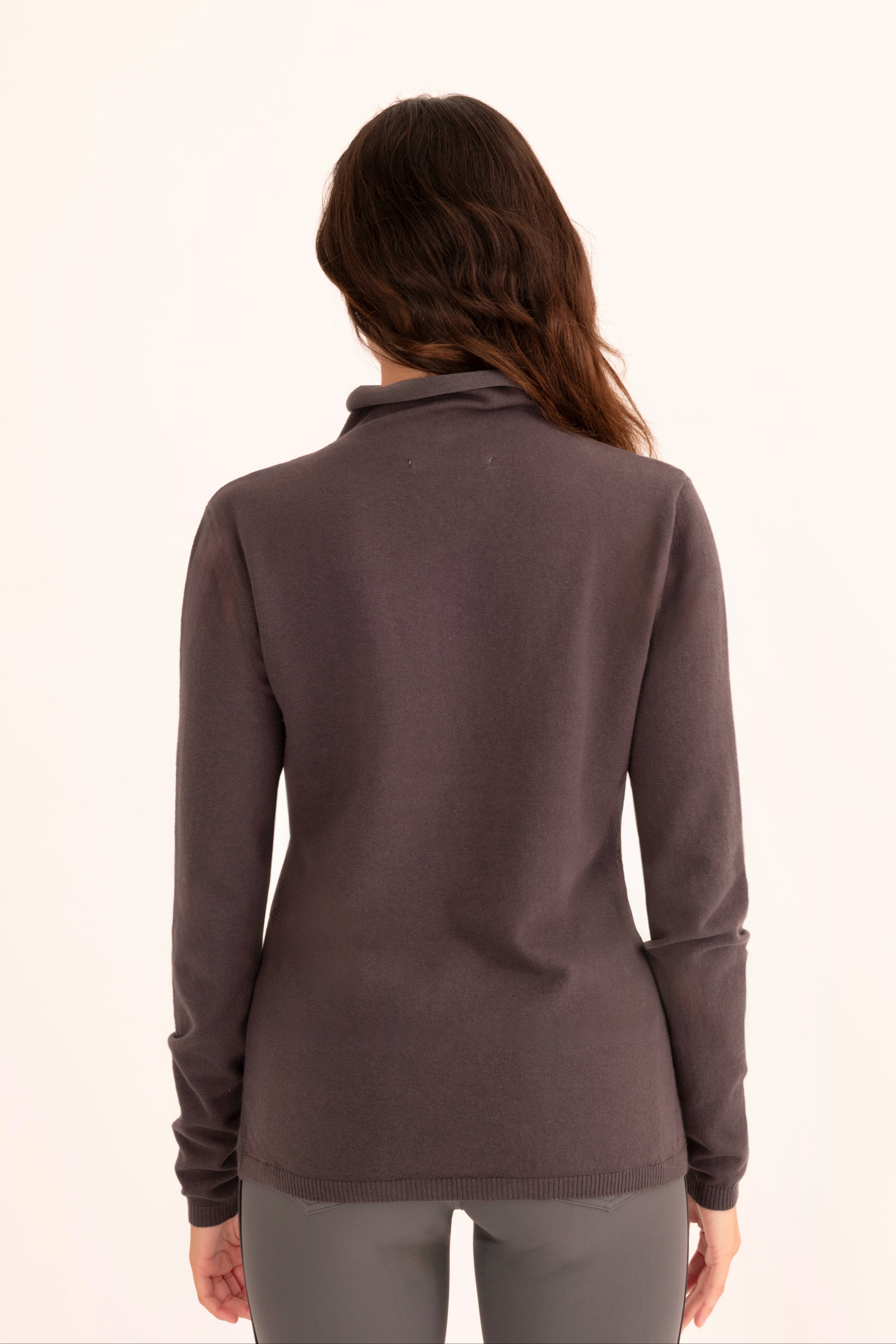 Back view of a woman wearing a gray funnel neck top and gray pants on a white background