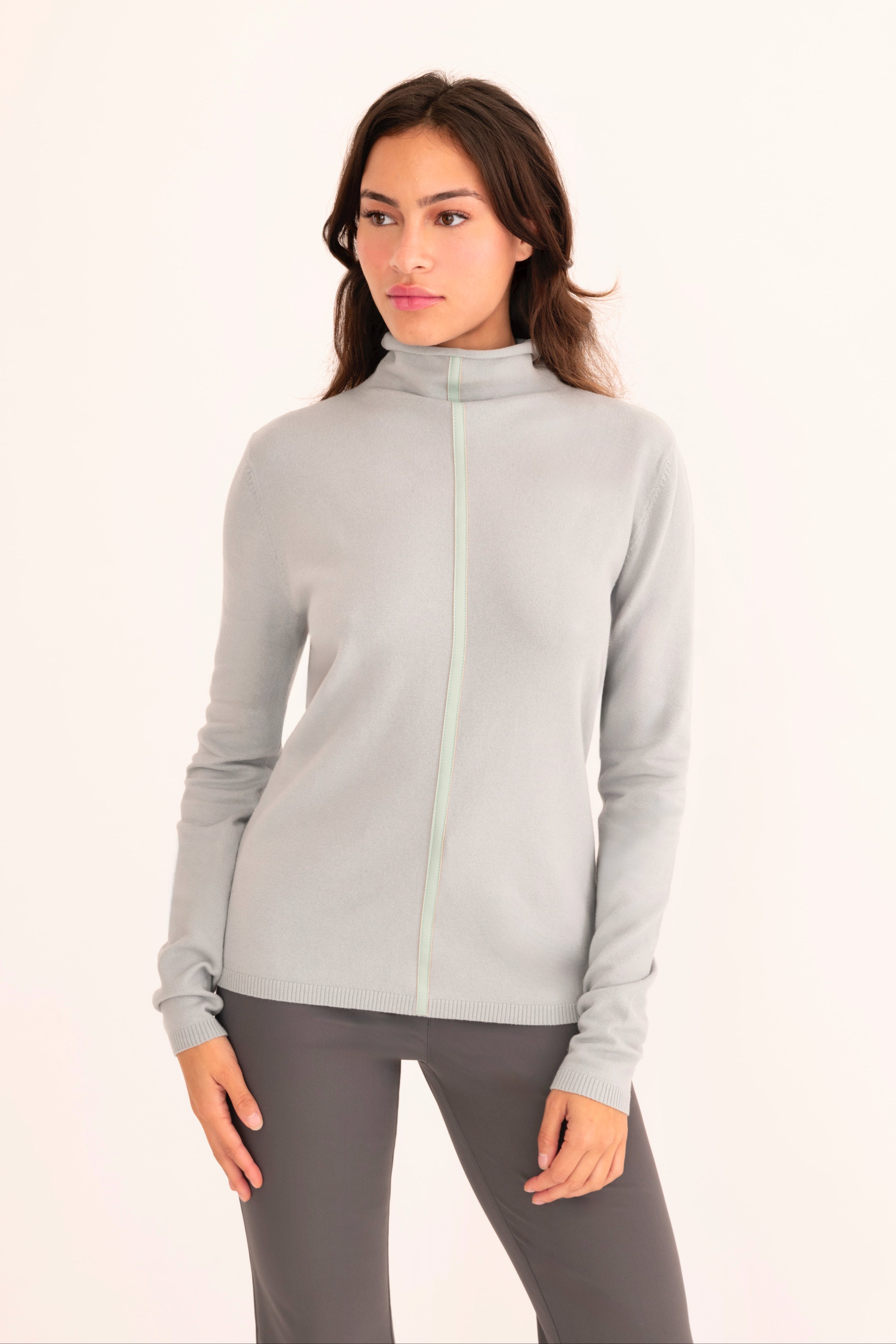Front view of a woman wearing a light blue funnel neck top and gray pants on a white background