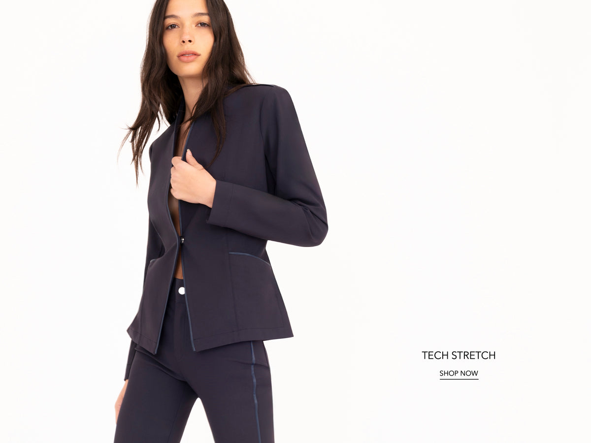 A woman modeling a dark navy blue tech-stretch blazer and matching pants against a clean white background, with text on the right reading 'TECH STRETCH SHOP NOW'.