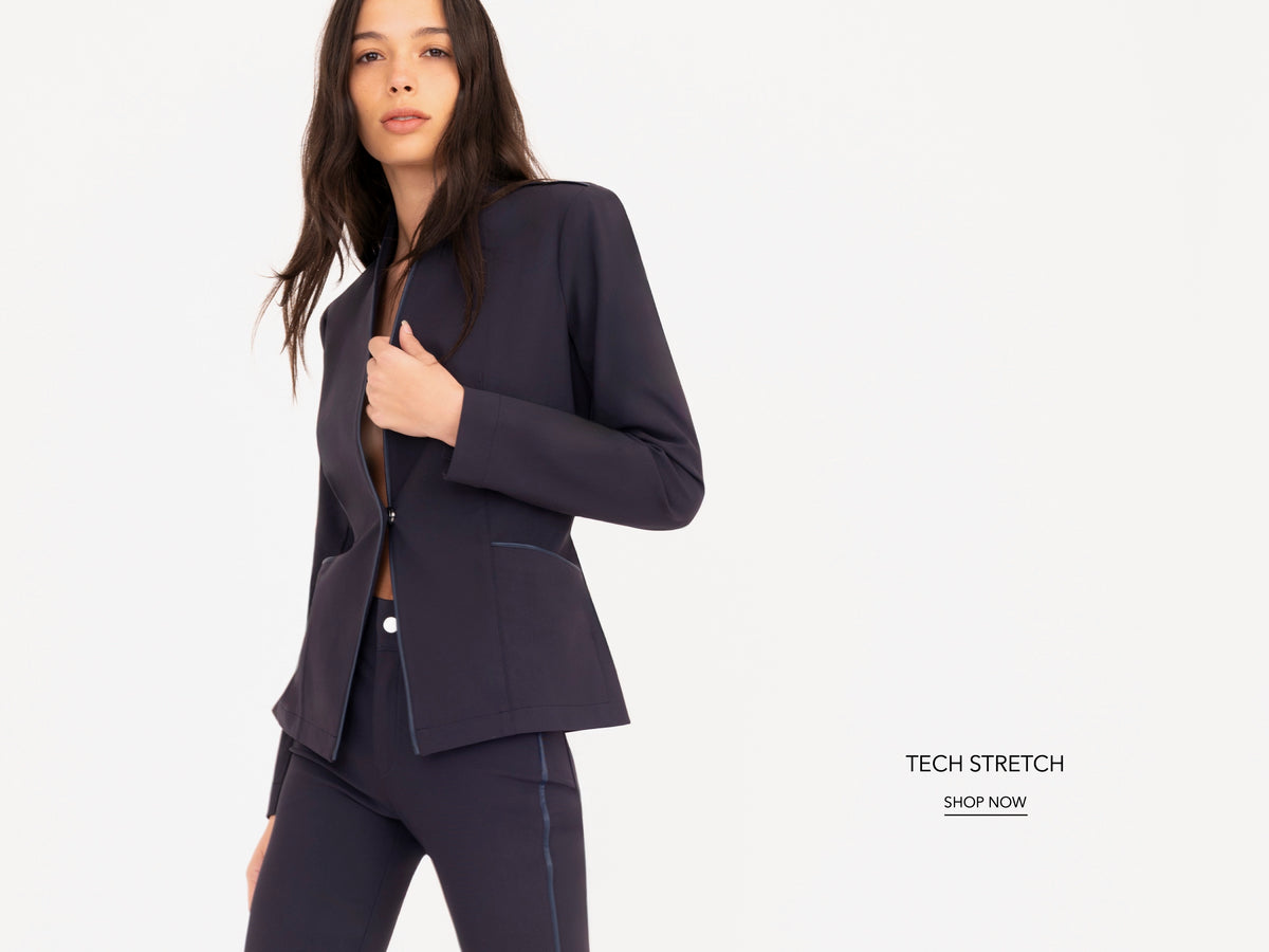 A woman modeling a dark navy blue tech-stretch blazer and matching pants against a clean white background, with text on the right reading 'TECH STRETCH SHOP NOW'.