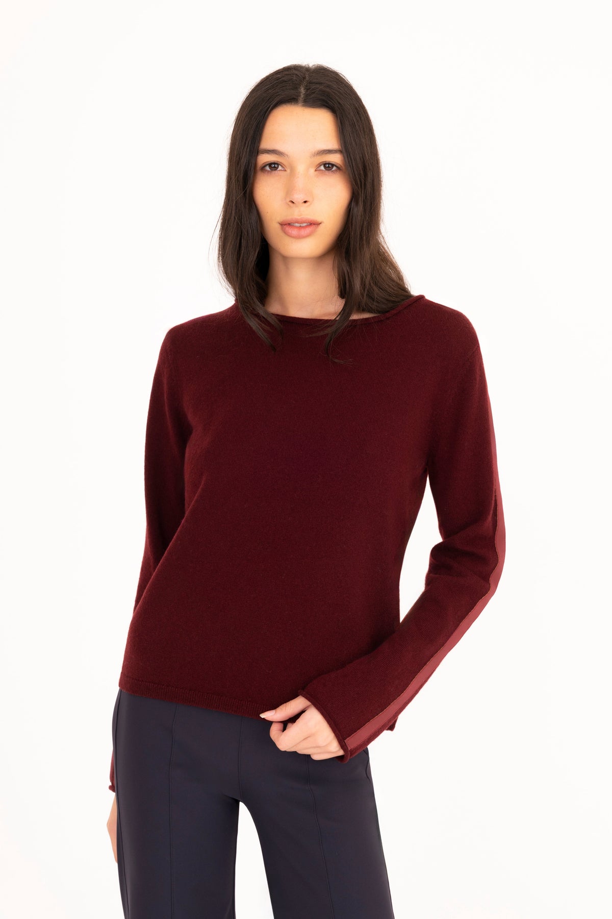 A woman modeling a burgundy long-sleeve knit sweater, paired with navy blue pants, against a plain white studio background.