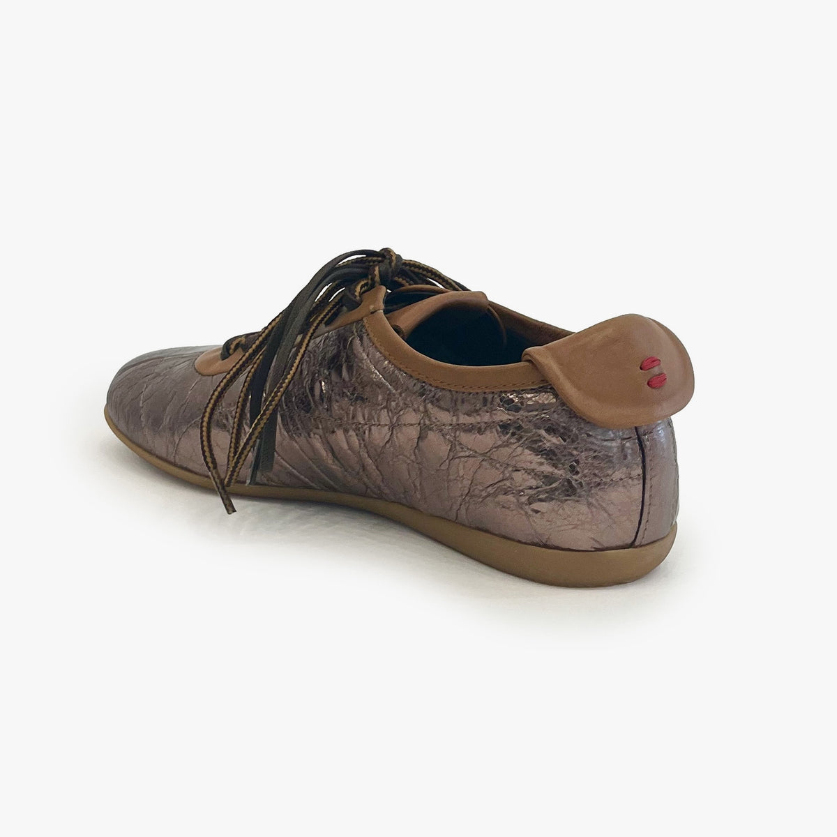 A single women's low-top shoe shown from a rear three-quarter angle on a light gray background. The shoe features a metallic bronze and brown textured upper, dark brown laces, a brown collar, and a tan sole.