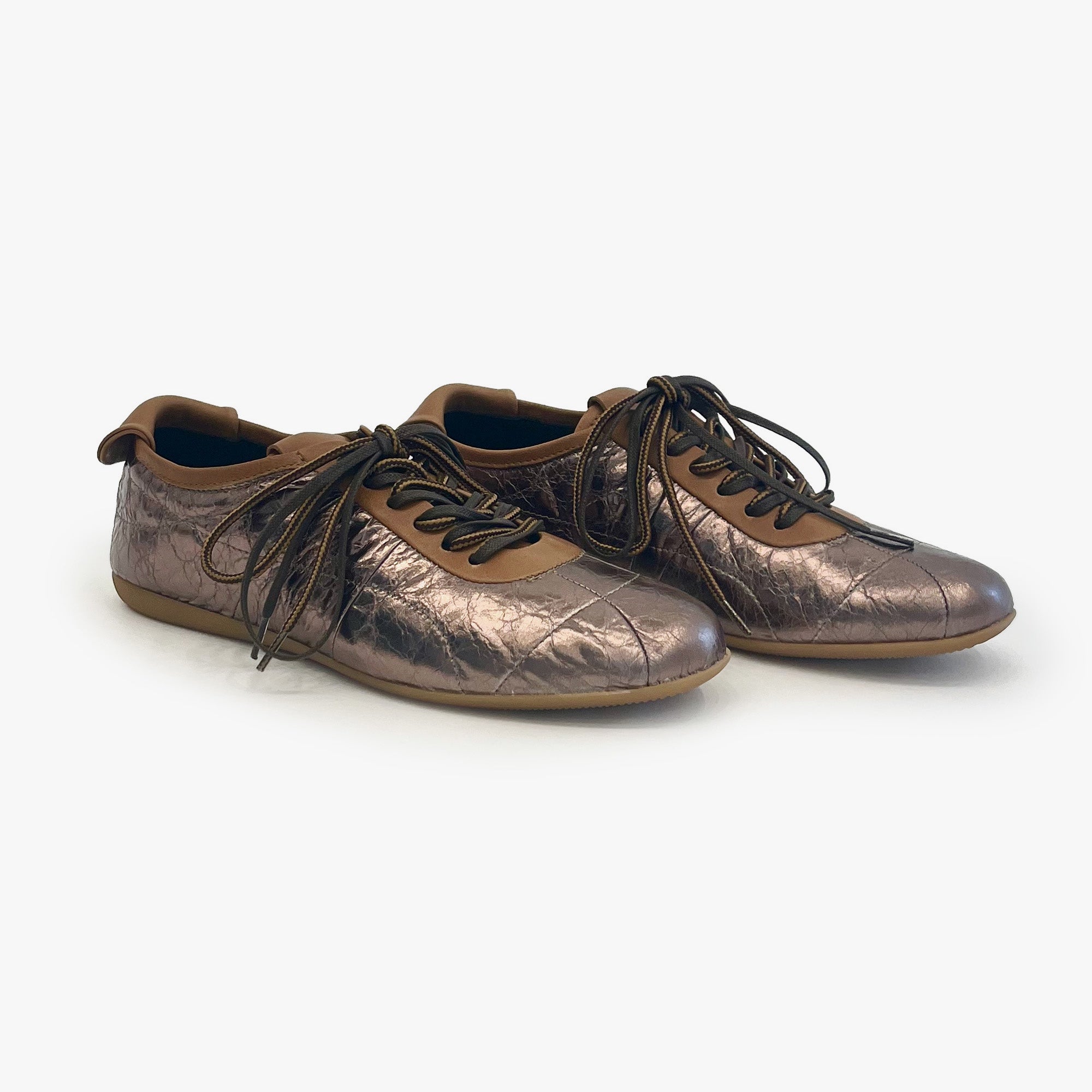 A pair of metallic bronze leather lace-up sneakers with a quilted toe cap and brown laces, shown on a light gray background.
