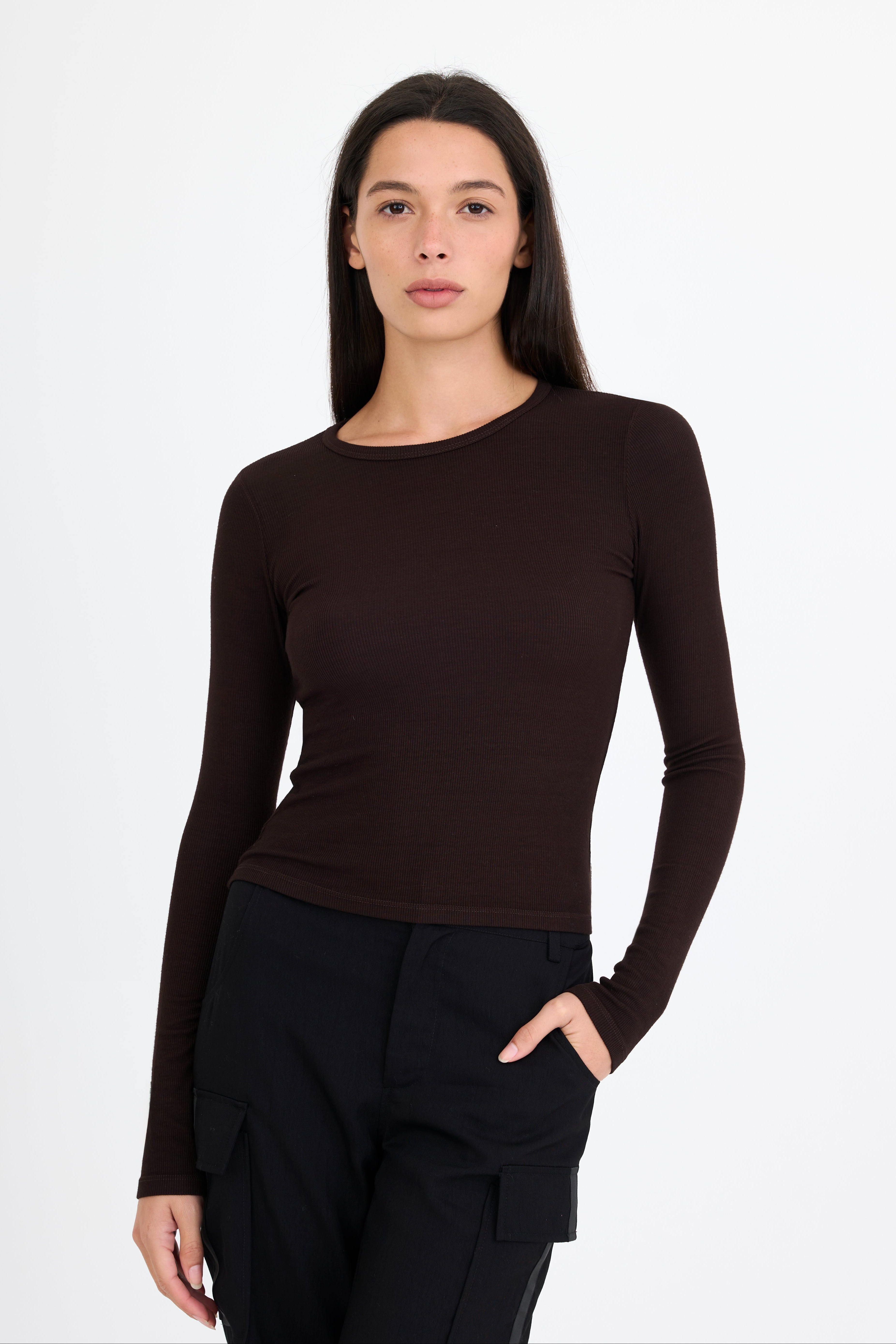 Woman wearing a brown long-sleeve t-shirt and black pants on a white background