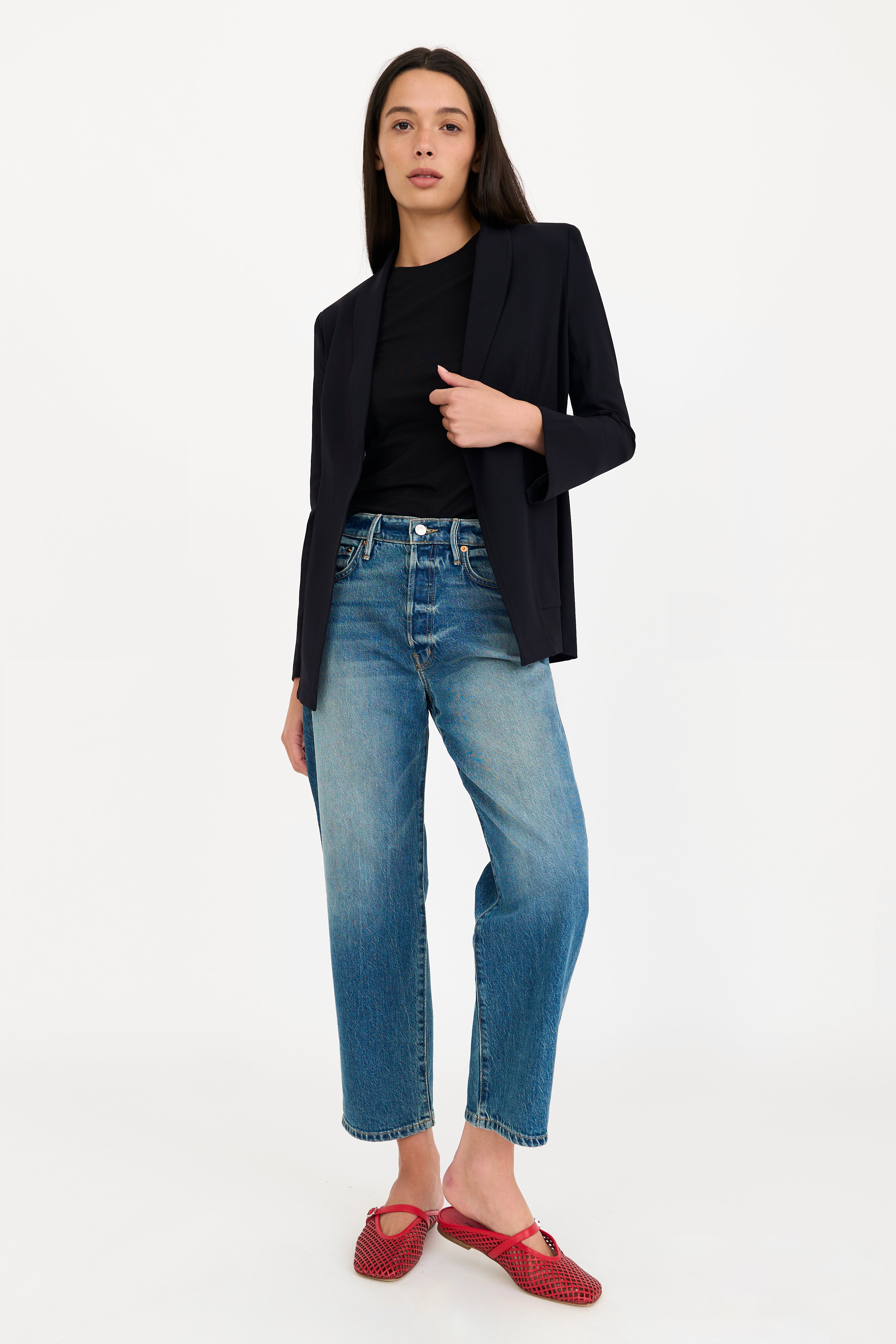 Woman wearing a black blazer, black top, and blue jeans on a white background