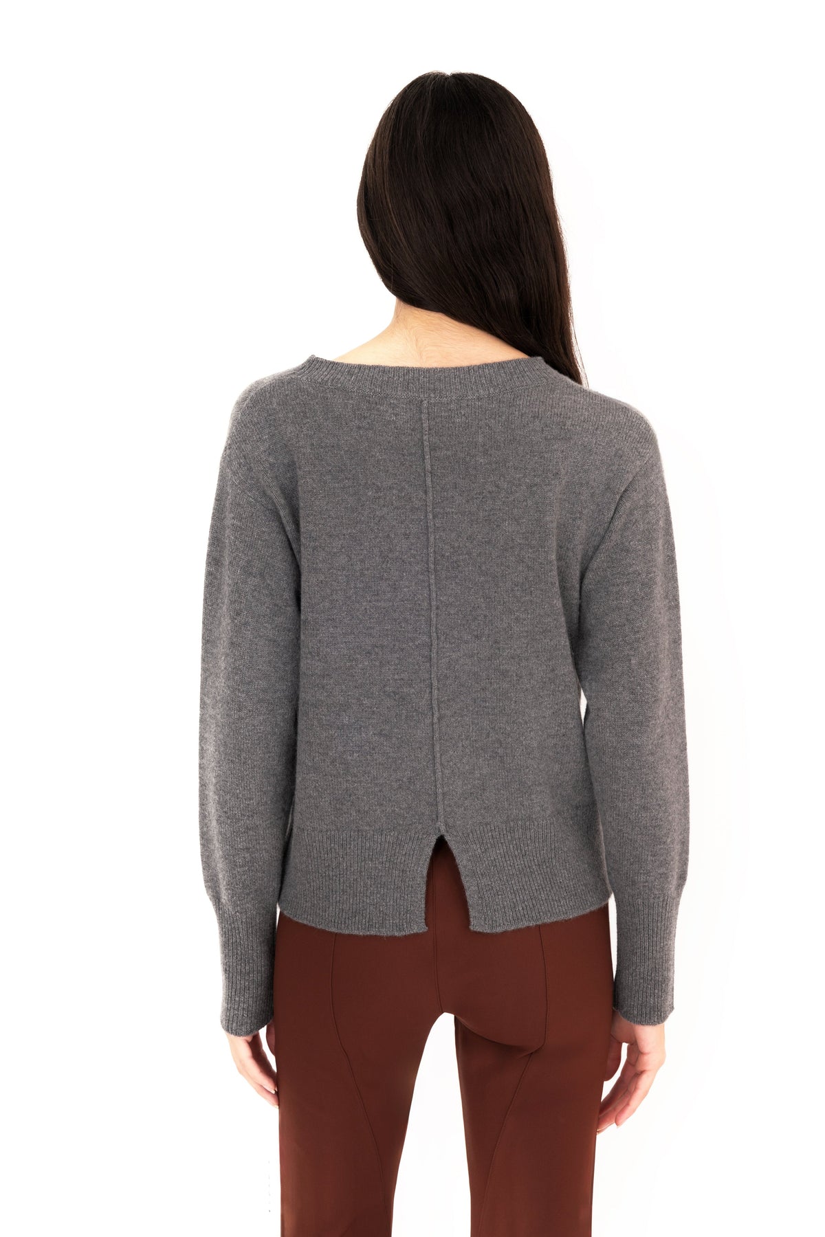 Back view of woman wearing a gray crew-neck sweater and dark brown pants on a white studio background.