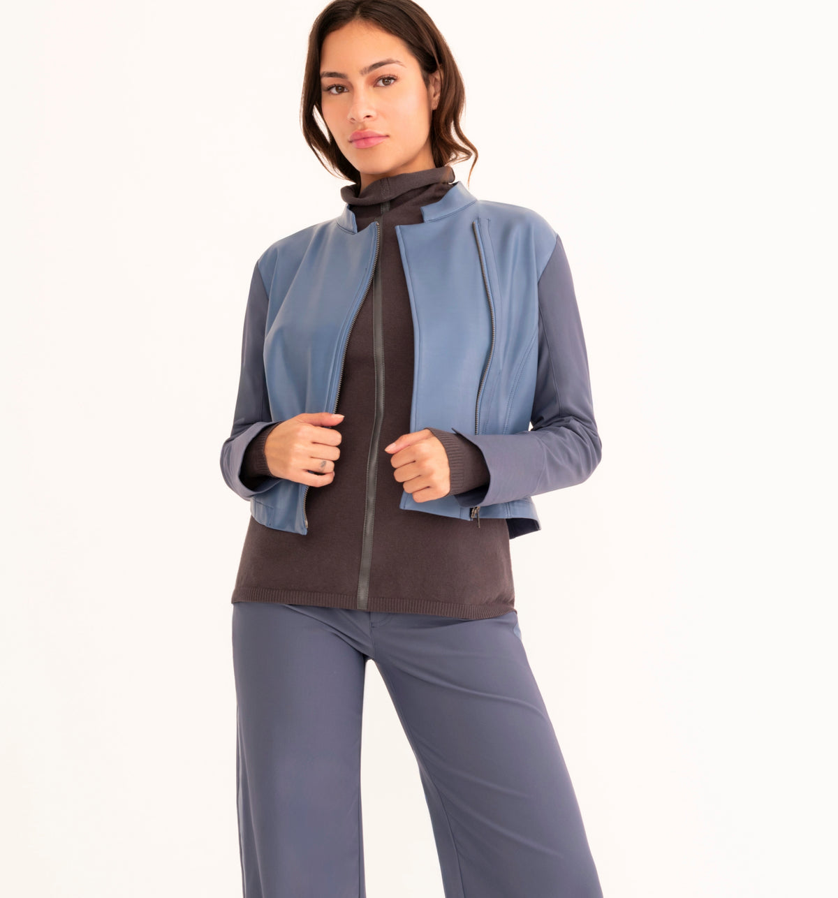 A woman modeling a light blue cropped zip-up jacket with contrasting dark gray sleeves, worn over a gray top and paired with matching gray pants, against a plain white studio background.