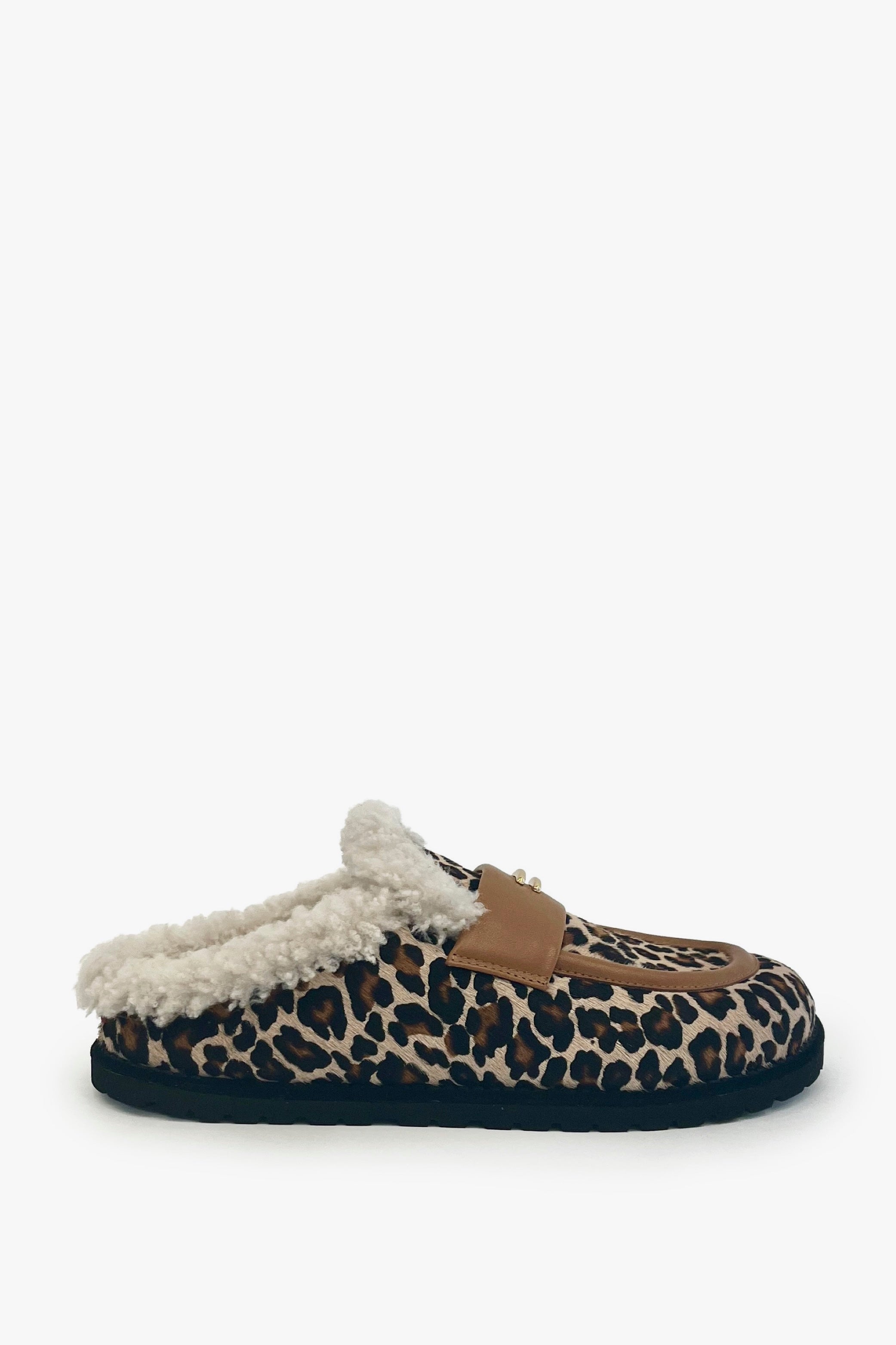 A single slip-on mule slipper featuring a brown, black, and beige leopard print pattern, a tan leather strap, and a fluffy white sherpa lining, shown against a plain white background.