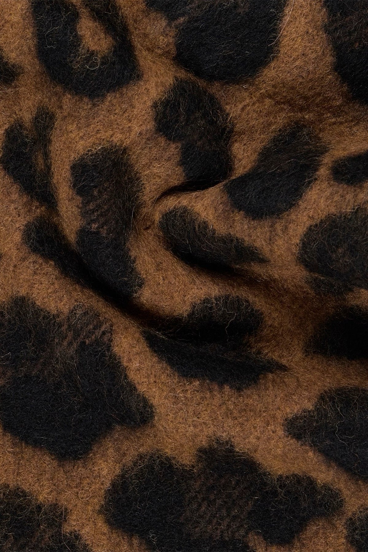 A close-up of a leopard-print shawl with a soft, fuzzy texture, showing a pattern of dark brown and black spots on a warm brown background.