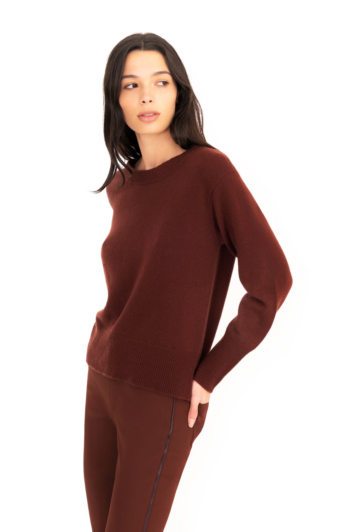 A woman modeling a dark brown knit crewneck sweater and matching brown pants against a plain white background.