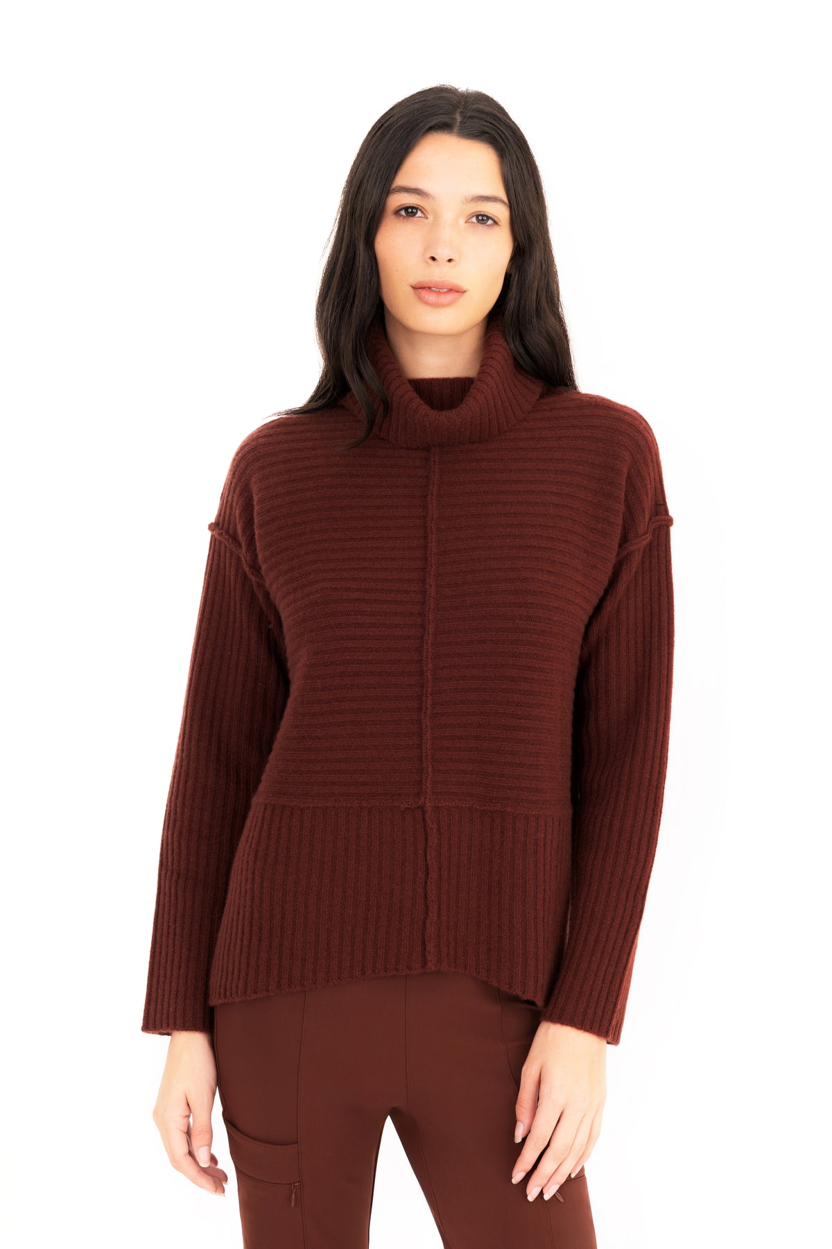 A woman modeling a ribbed knit funnel-neck sweater in a deep burgundy brown color, paired with matching pants, against a solid white background.