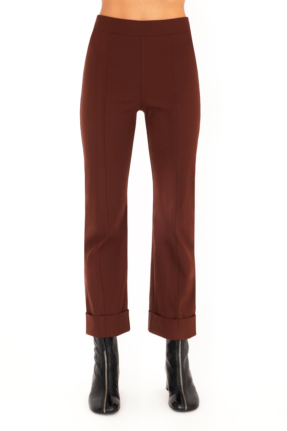 A model wearing dark brown cropped pants with rolled cuffs and black ankle boots, shown from the waist down on a white studio background.