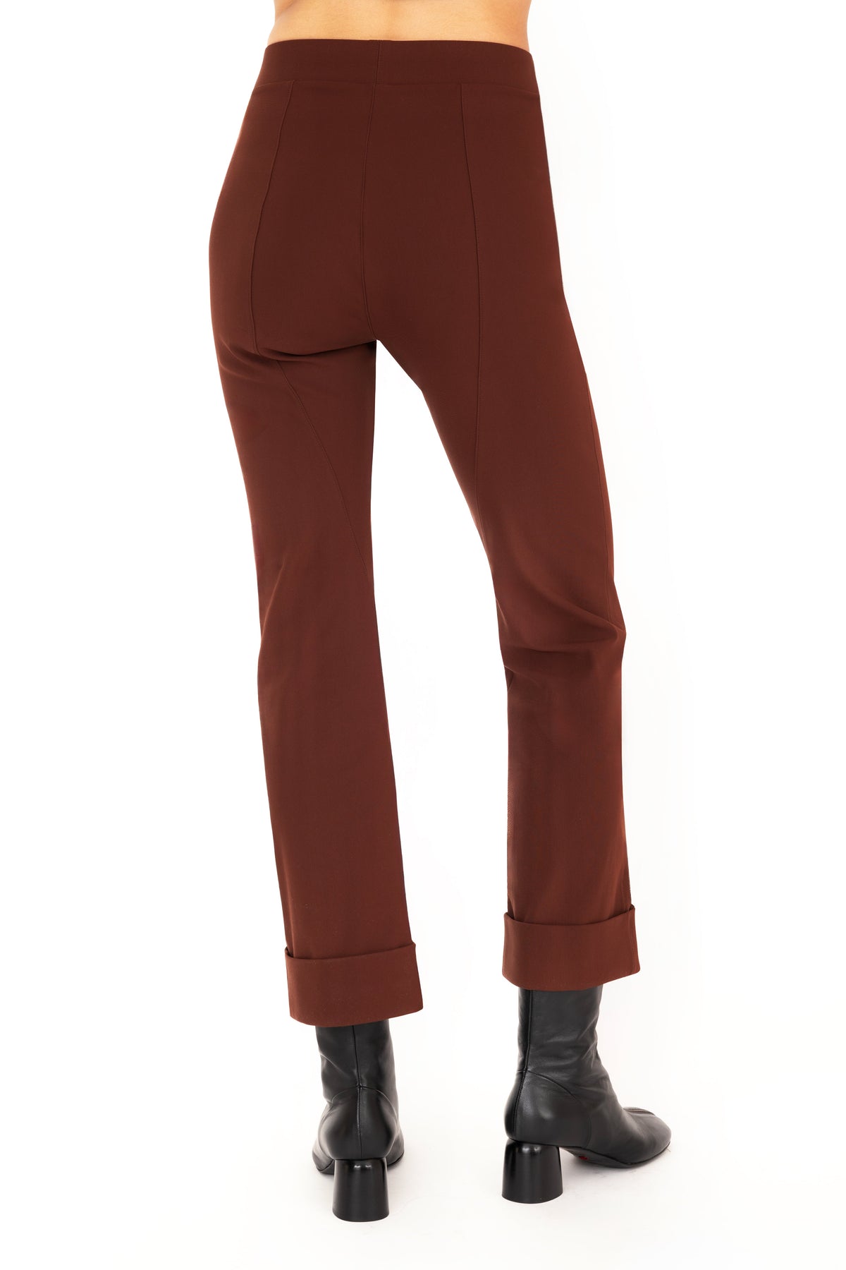 A model wearing dark brown cropped pants with rolled cuffs and black ankle boots, shown from the waist down on a white studio background.