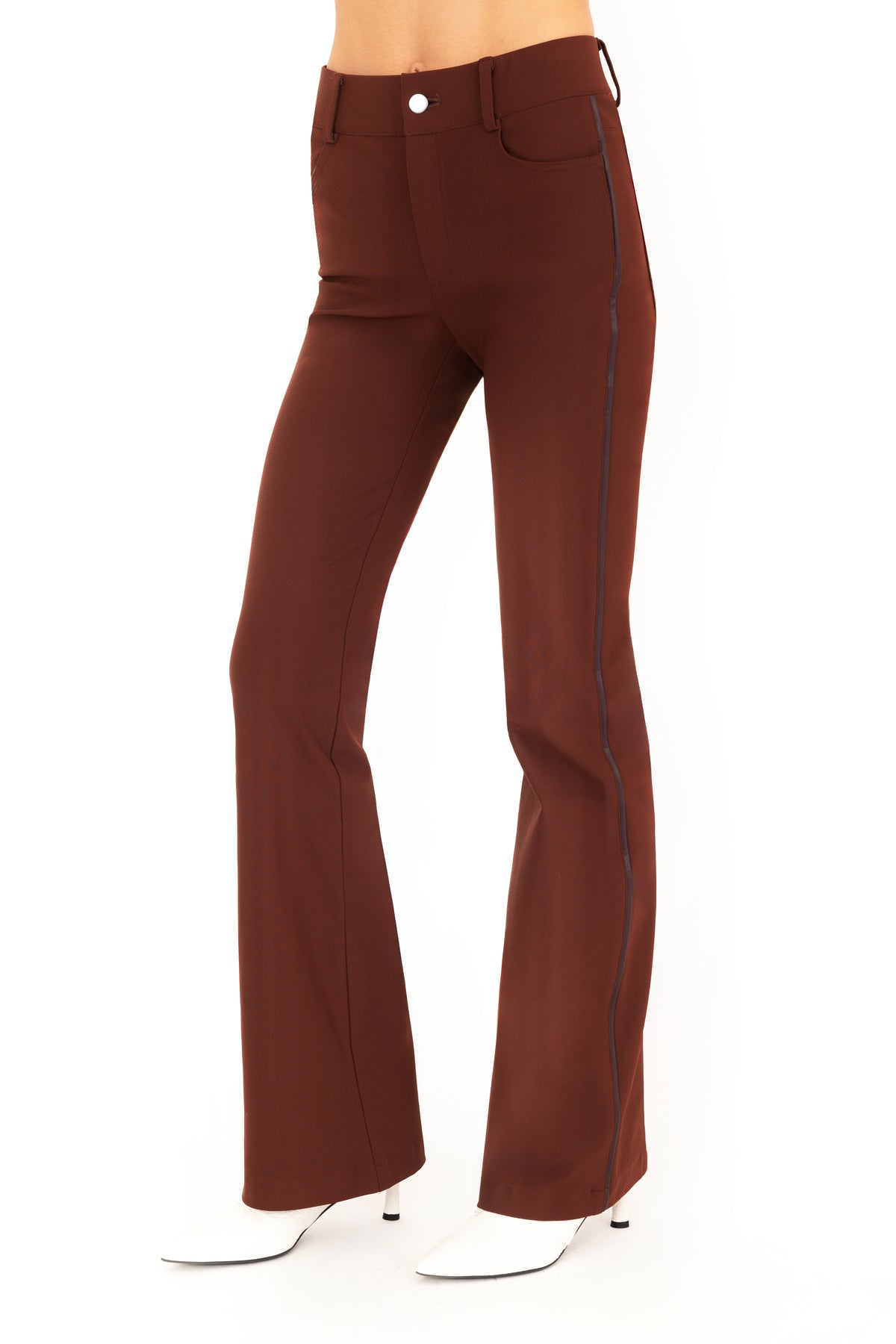 A pair of dark brown flare jean pants shown on a model from the waist down, paired with white pointed-toe boots against a plain white background.