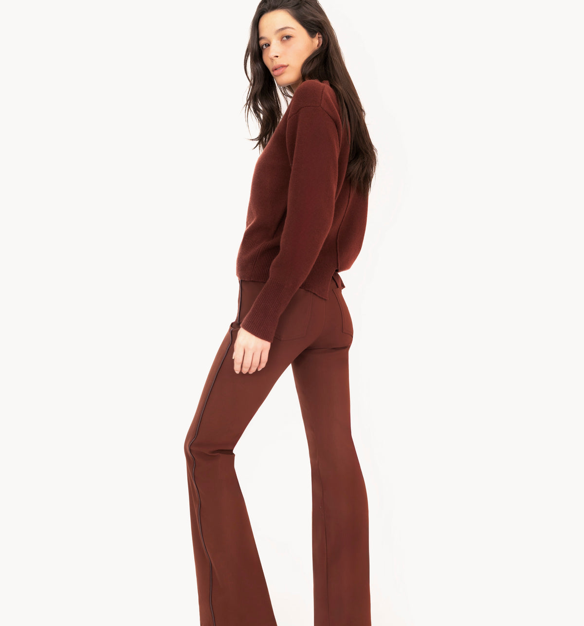 Woman wearing brown cashmere sweater and flare jean pants against a white studio background.