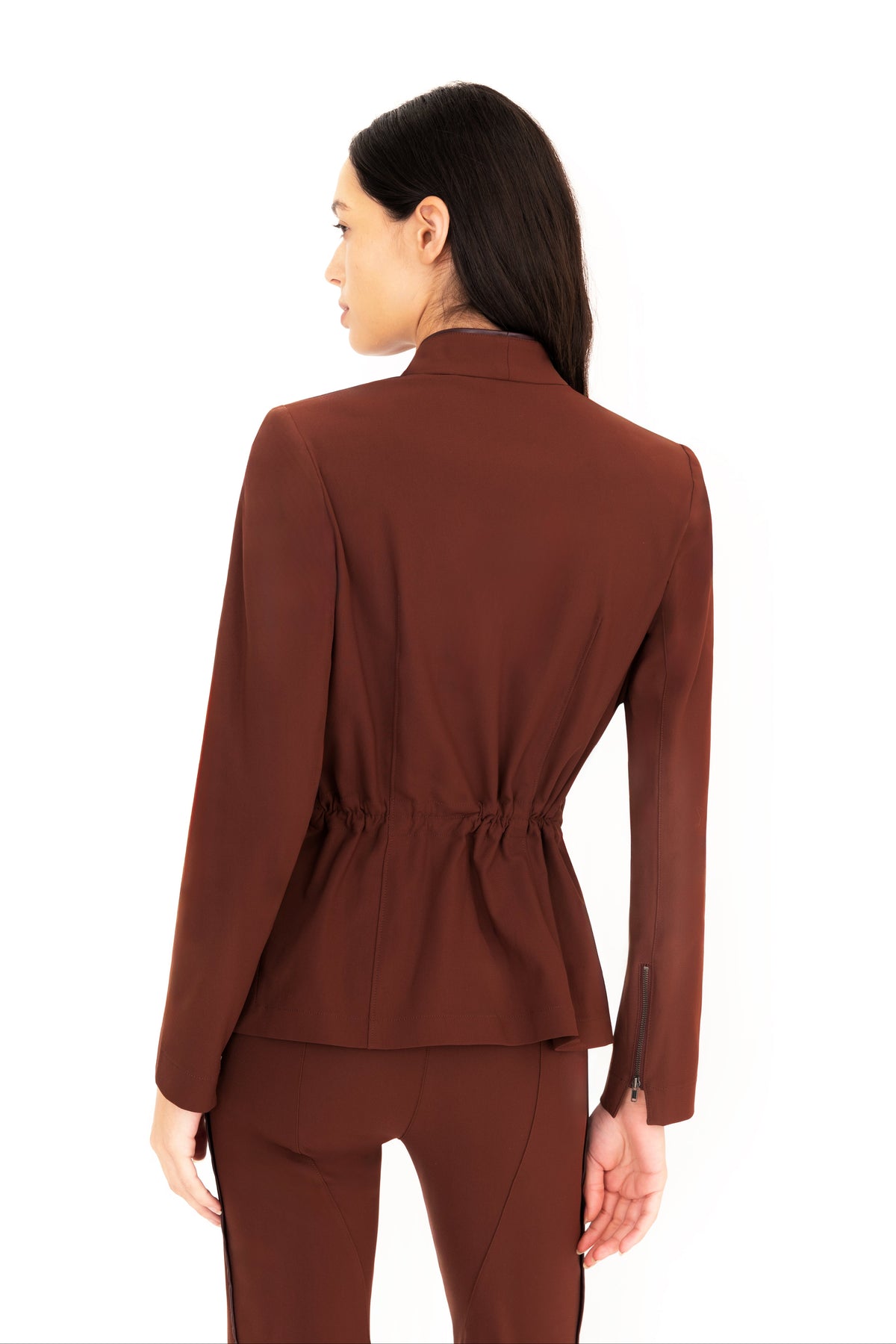 A woman shown from the back wearing a brown tailored blazer with a gathered waist and matching brown pants, photographed against a plain white studio background.