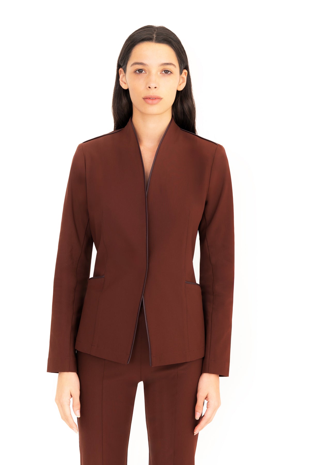 A woman modeling a matching brown structured blazer and trousers set against a plain white background.