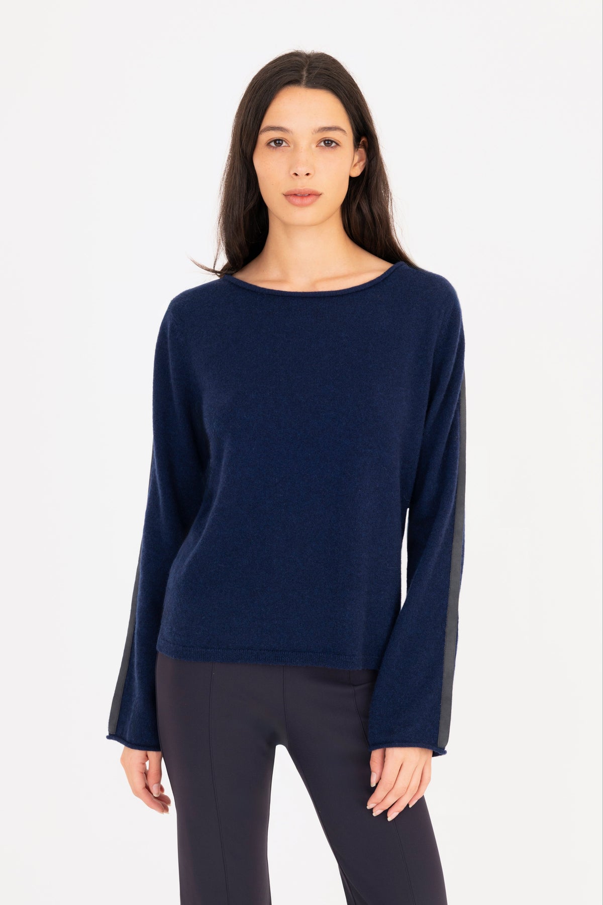 A woman modeling a navy blue long-sleeve knit sweater, paired with navy blue pants, against a plain white studio background.