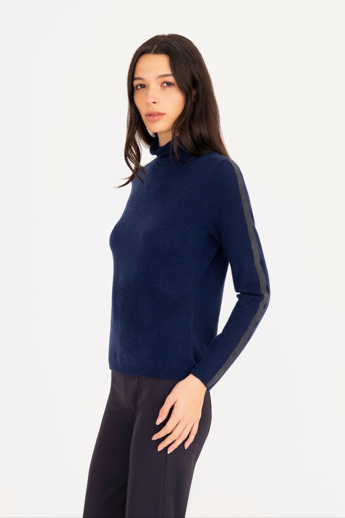 A woman modeling a navy blue mock neck knit sweater, paired with navy blue trousers, against a plain white studio background.
