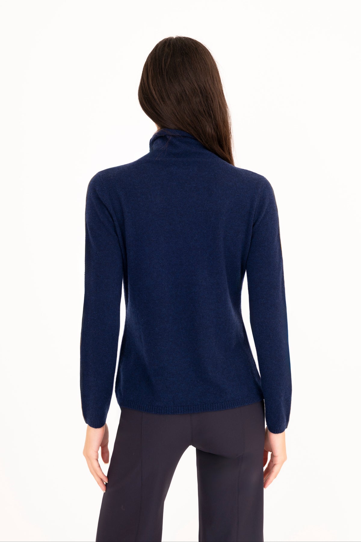 A woman viewed from the back wearing a navy blue mock neck sweater and navy blue trousers against a plain white background.