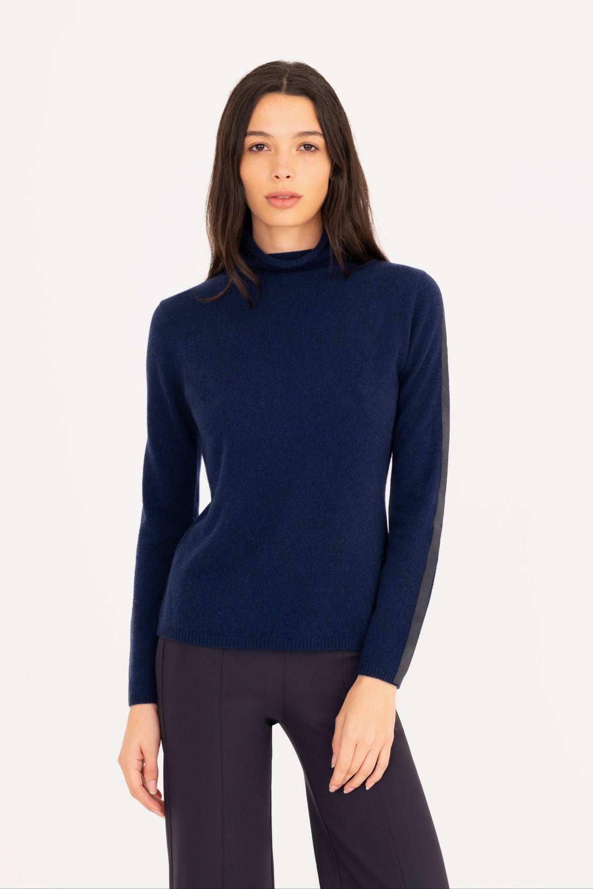 A woman modeling a navy blue mock neck knit sweater, paired with navy blue trousers, against a plain white studio background.