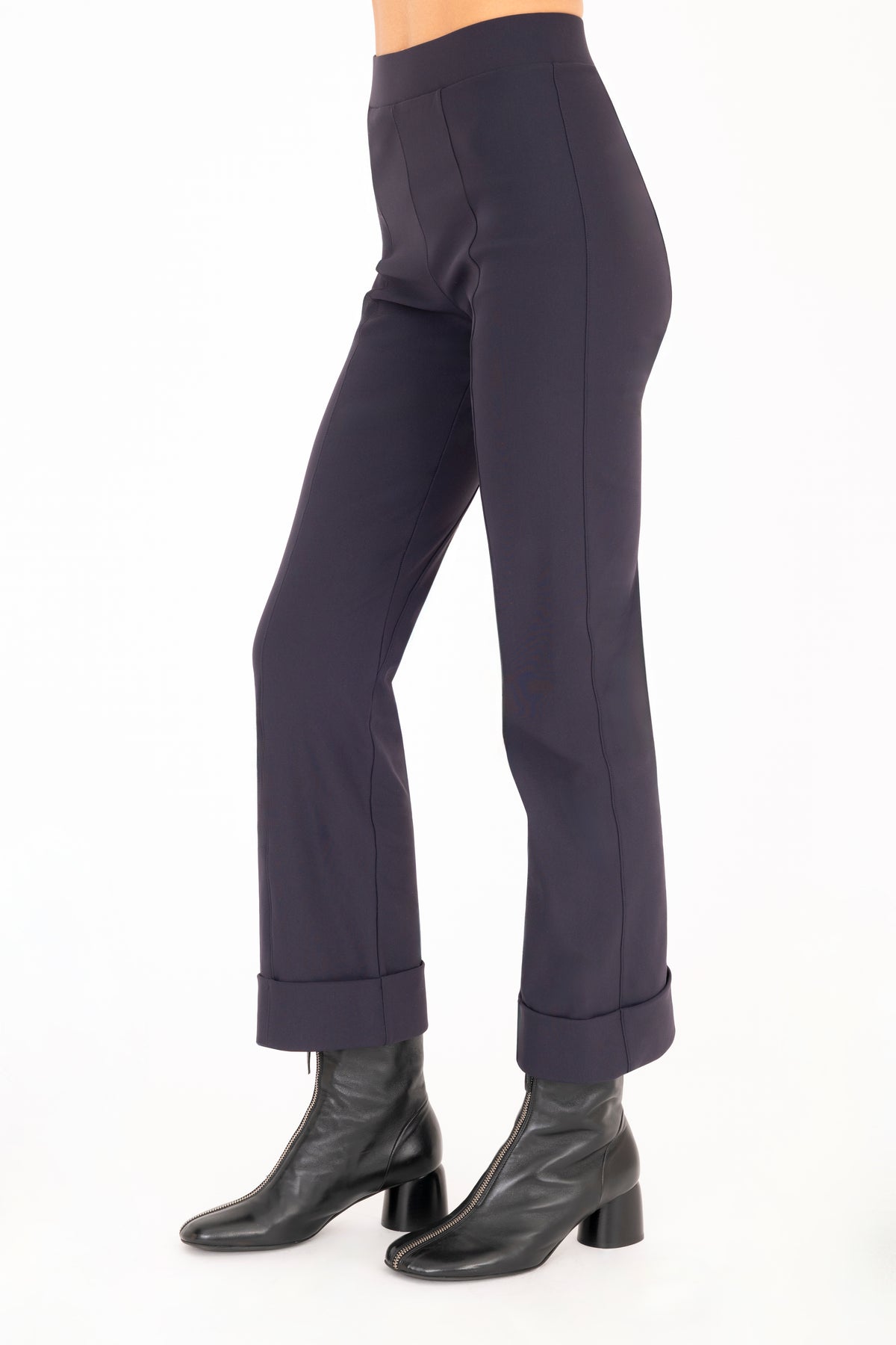 A model wearing dark navy cropped pants with rolled cuffs and black ankle boots, shown from the waist down on a white studio background.