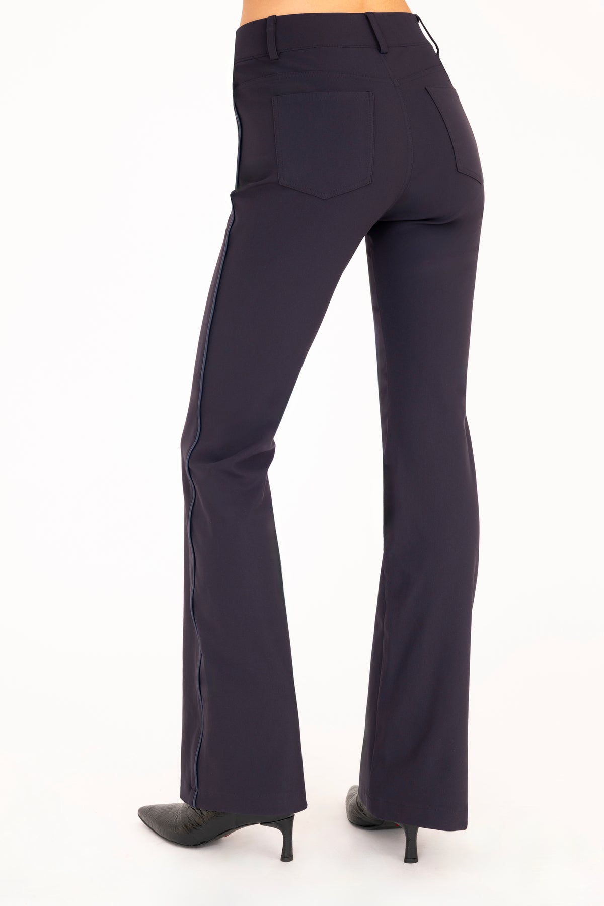 A pair of dark blue flare jean pants shown on a model from the waist down, paired with black pointed-toe boots against a plain white background.