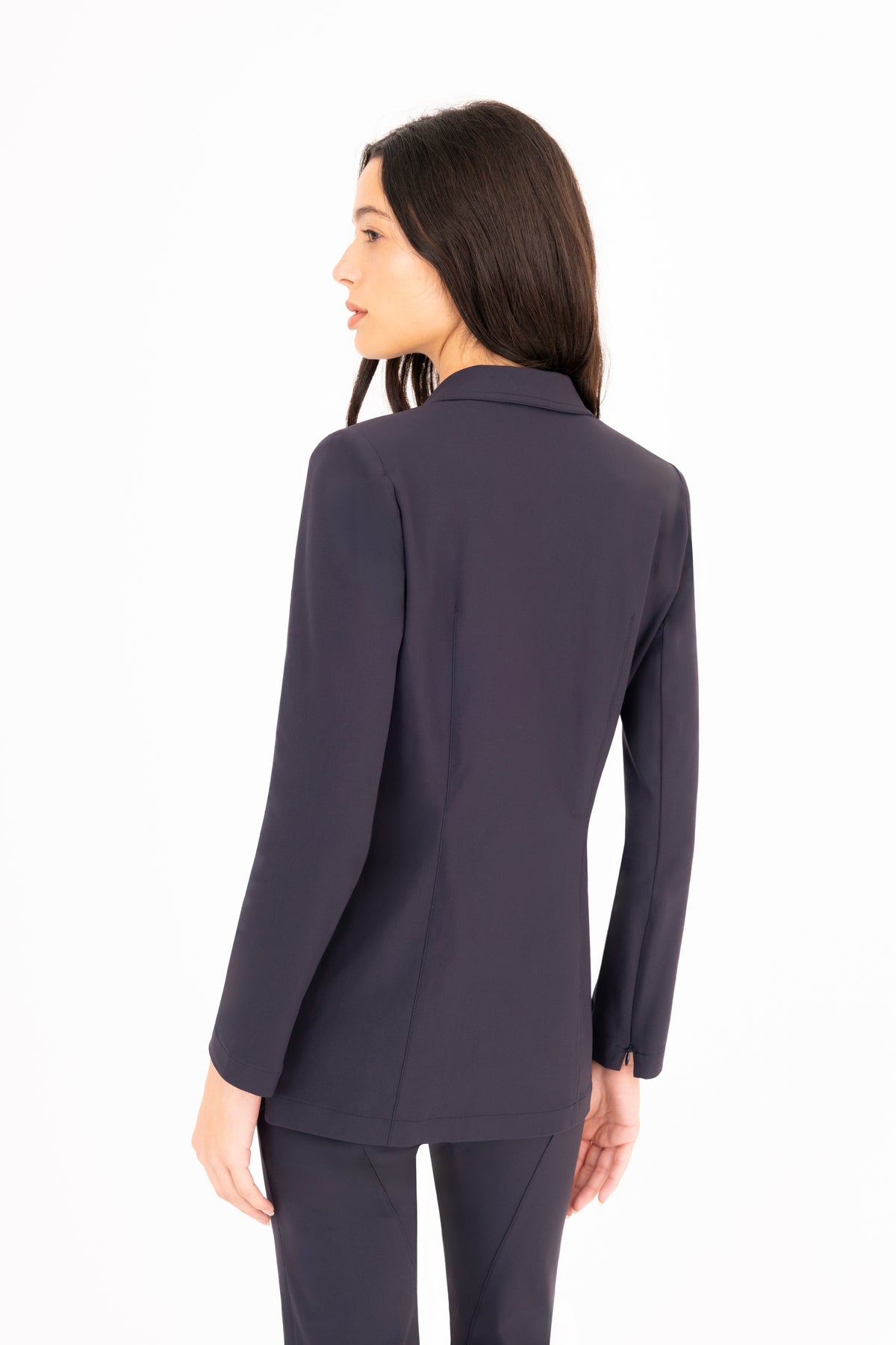 A woman viewed from the back wearing a tailored navy blue blazer with matching trousers against a plain white studio background.