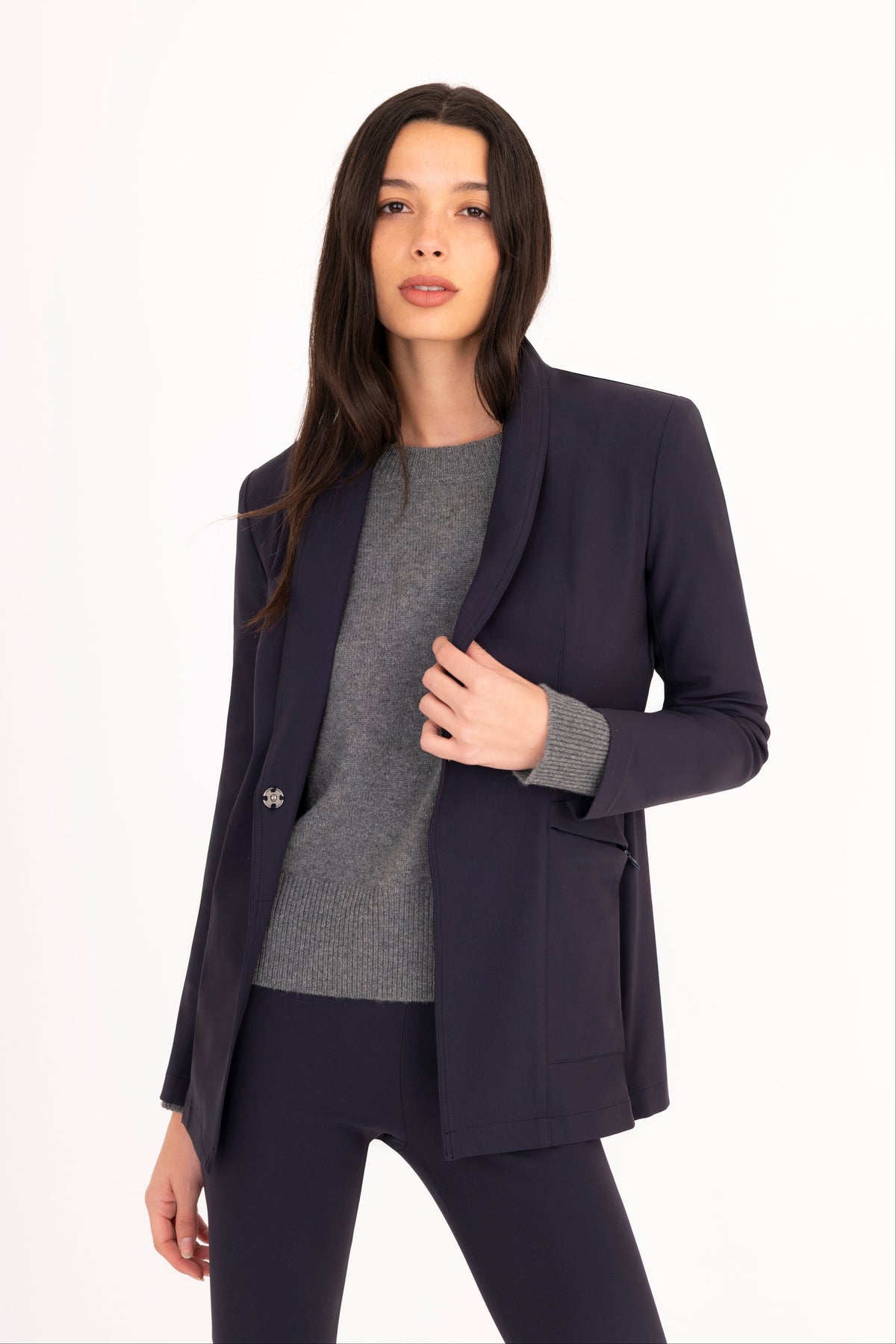 A woman modeling a matching navy blue tailored blazer and trousers set with a gray cashmere sweater against a plain white studio background.