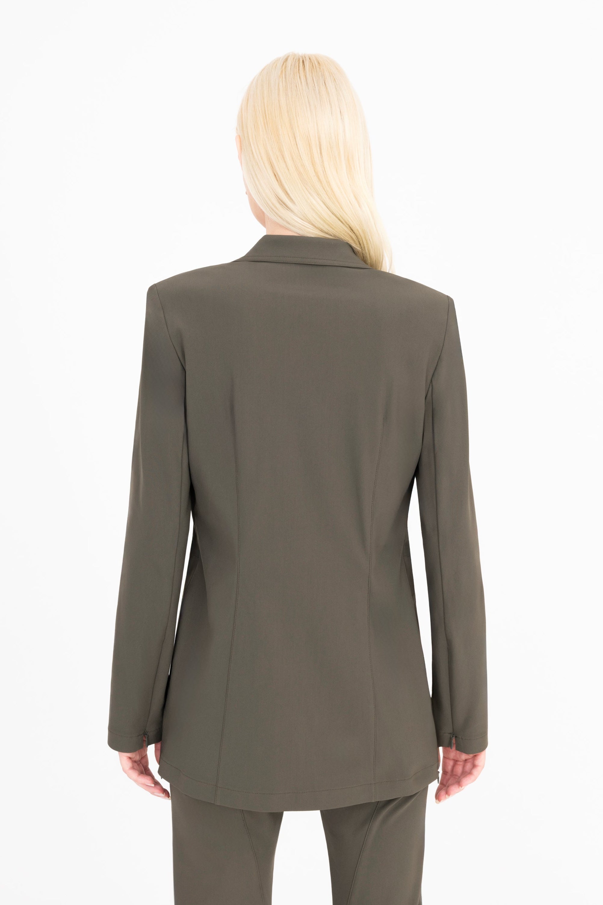 A woman viewed from the back wearing a tailored olive green blazer and matching trousers against a plain white studio background.