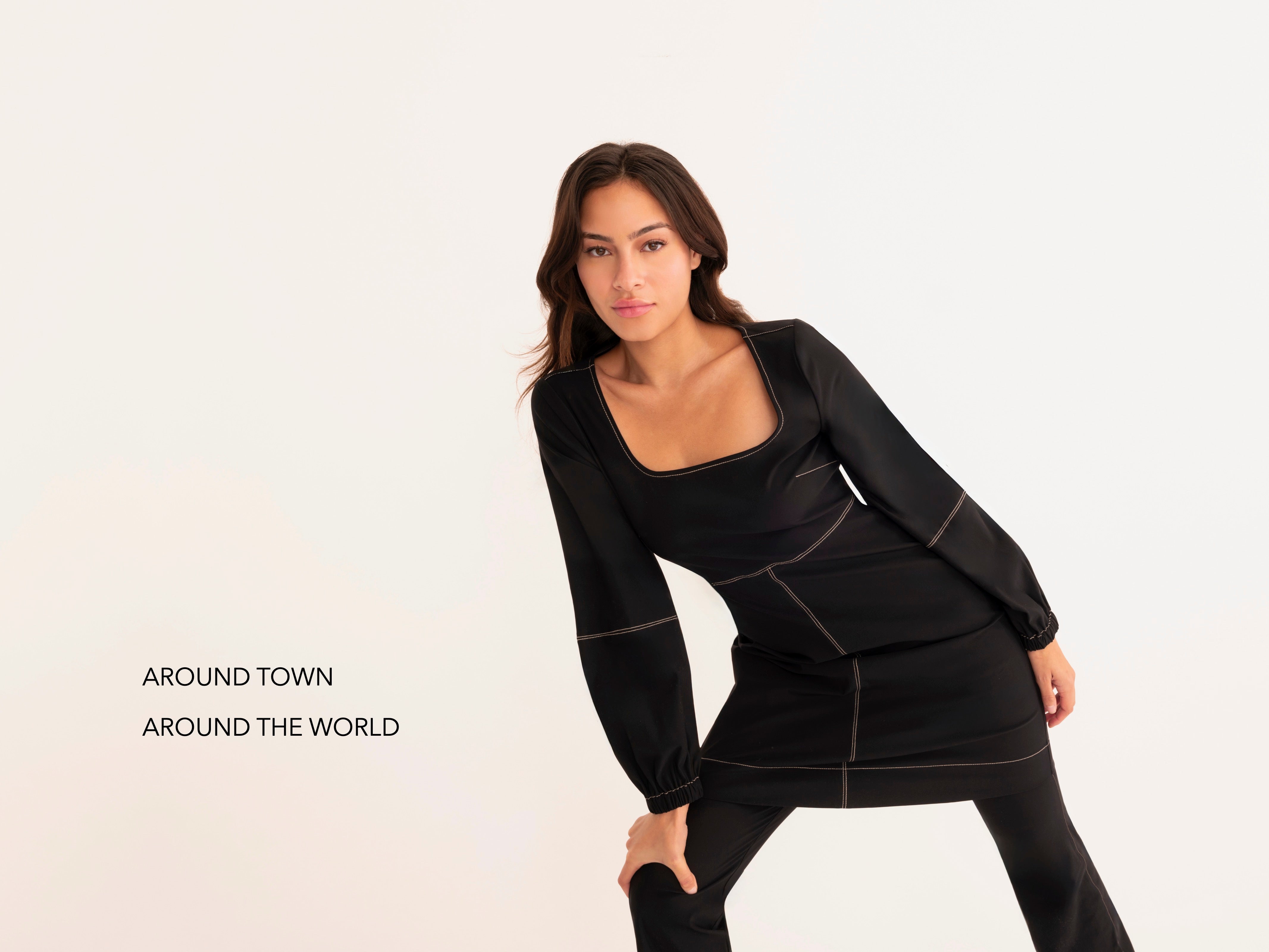 A woman modeling a black long-sleeve dress with contrasting light stitching details, posed against a clean white studio background with the text 'AROUND TOWN AROUND THE WORLD' on the left.