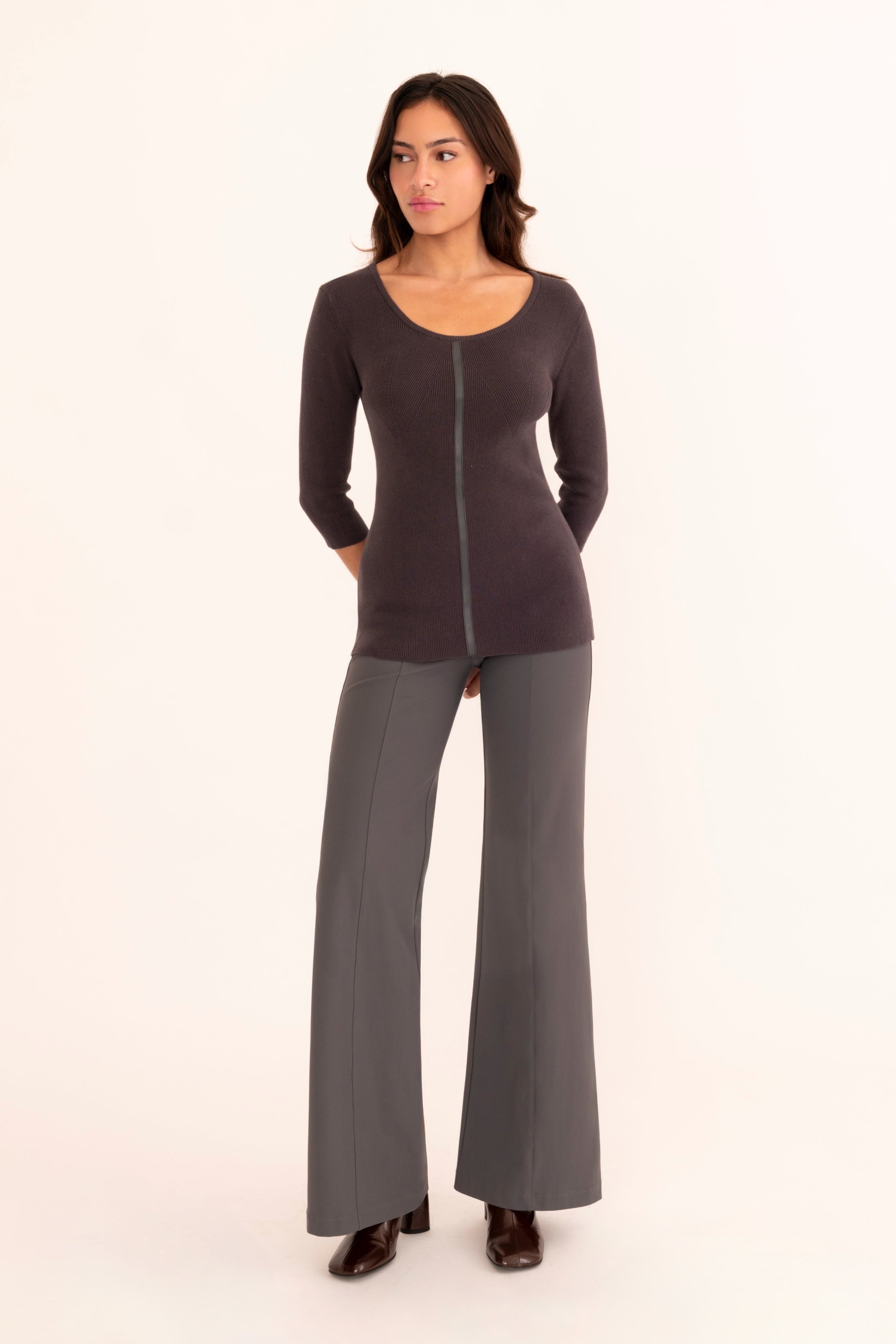 A woman modeling a gray three-quarter sleeve top paired with gray  pants and brown boots, standing against a solid white background.