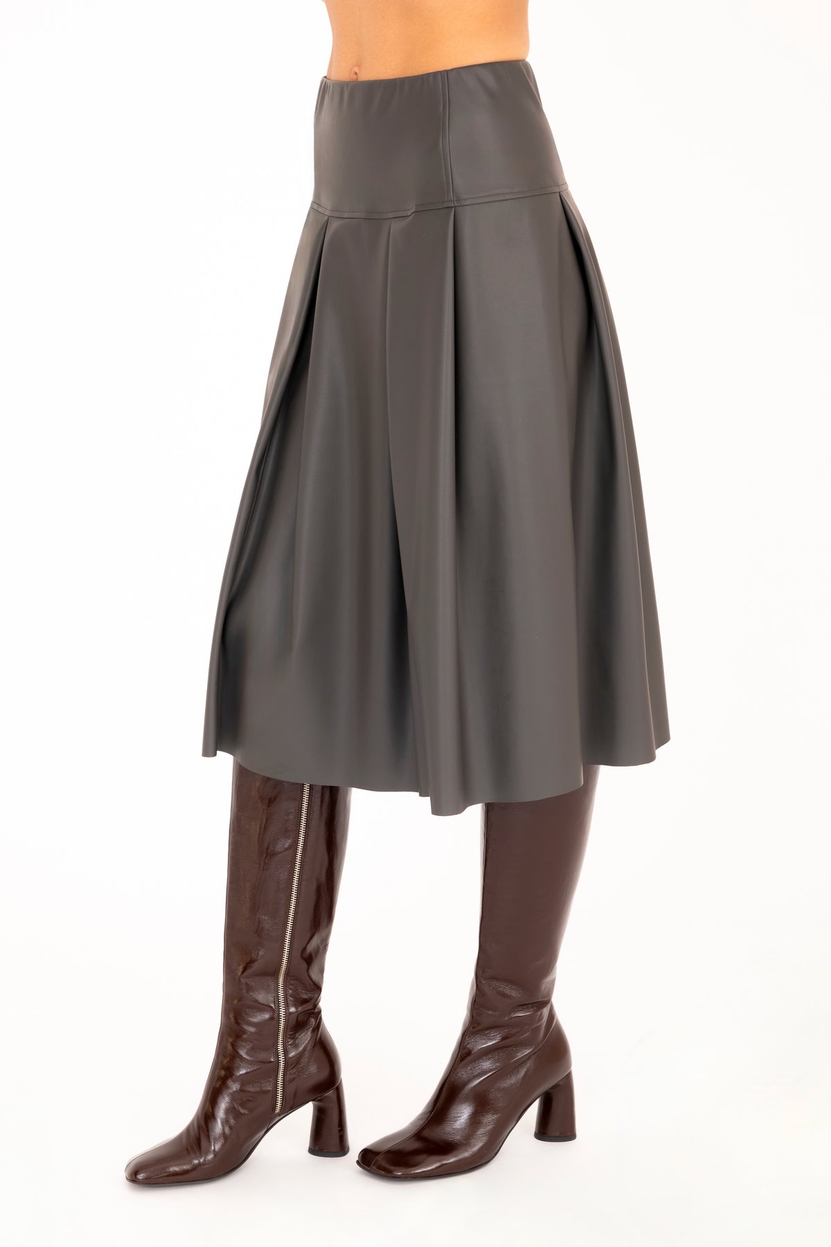 A gray vegan leather pleated A-line skirt shown on a model from the waist down, paired with dark brown knee-high leather boots against a plain white background.