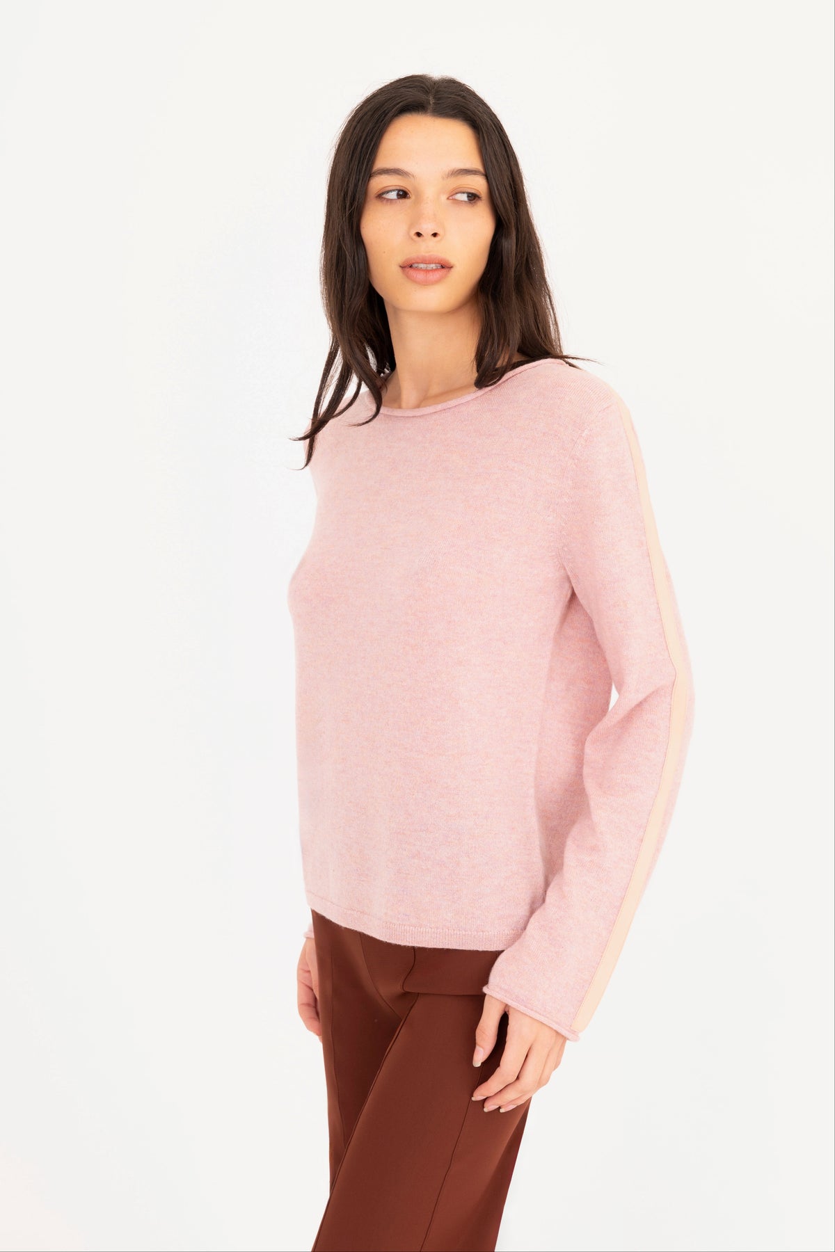 A woman modeling a pink long-sleeve knit sweater, paired with brown pants, against a plain white studio background.