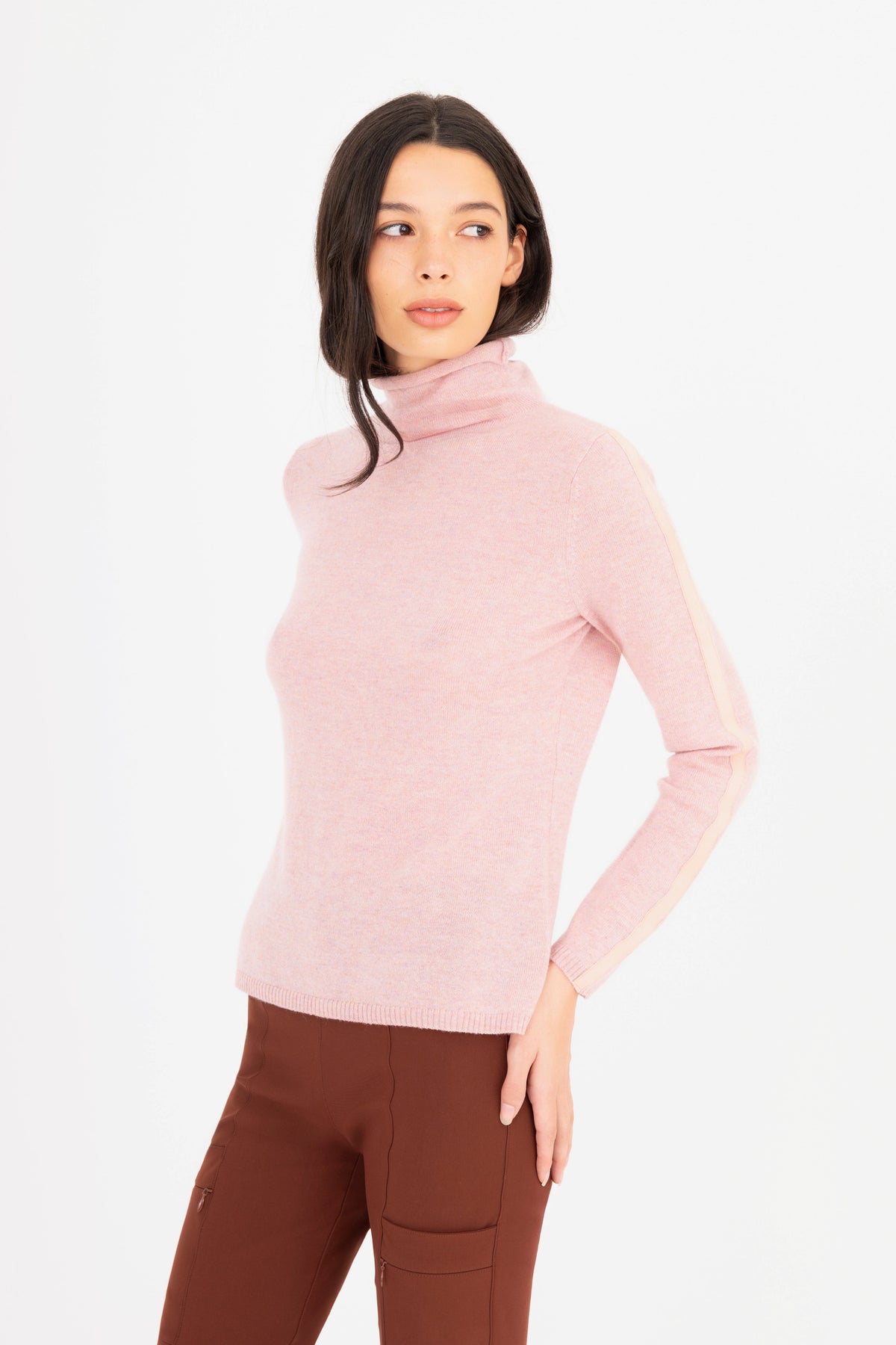 Woman wearing a light pink turtleneck sweater and brown pants on a white background