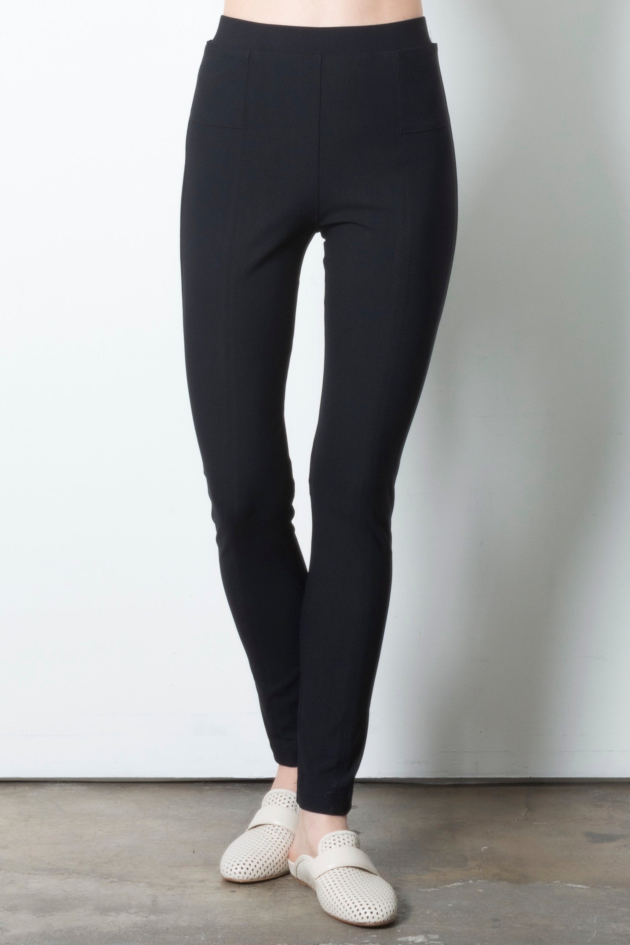 Person wearing black leggings with white shoes on a plain background